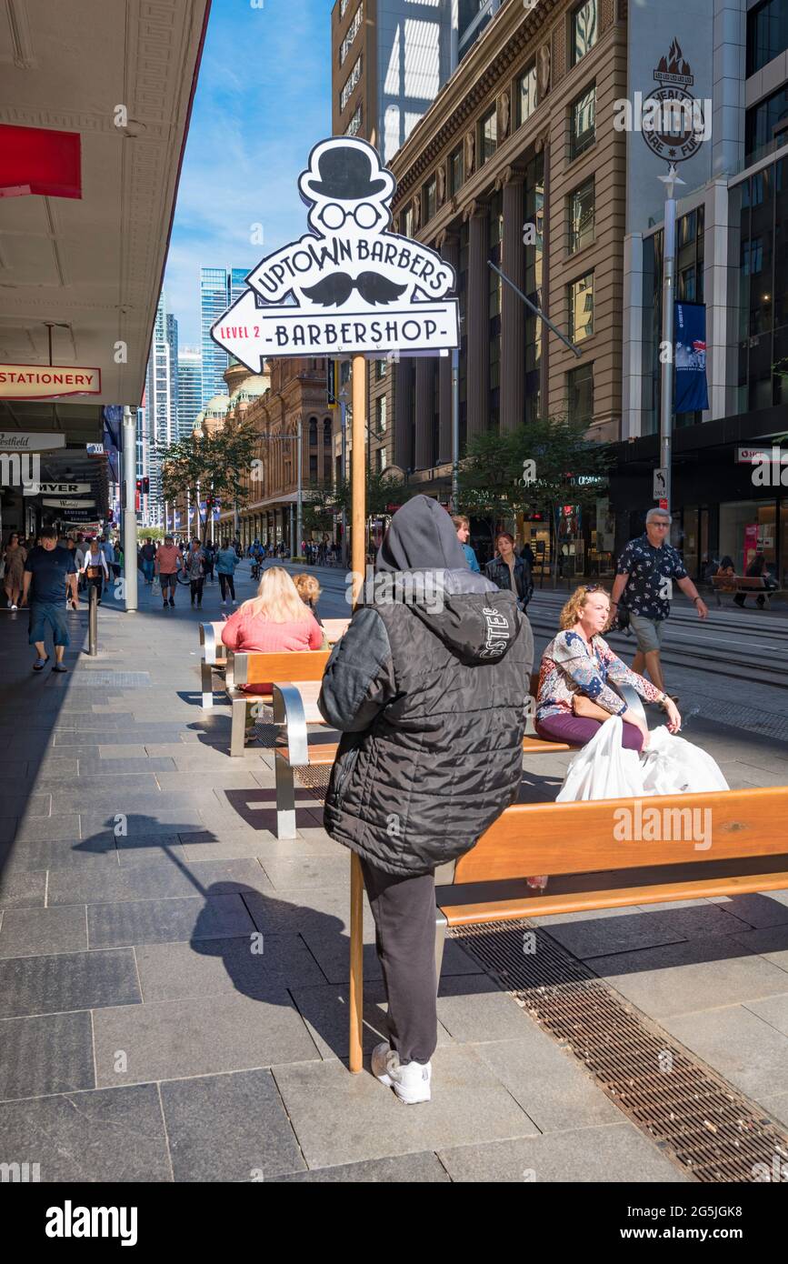 Eine Person, die ein Pole-Banner oder eine Werbung für einen Friseur hält, während sie ihr Telefon in der Pitt Street Mall, Sydney, Australien, ansieht Stockfoto