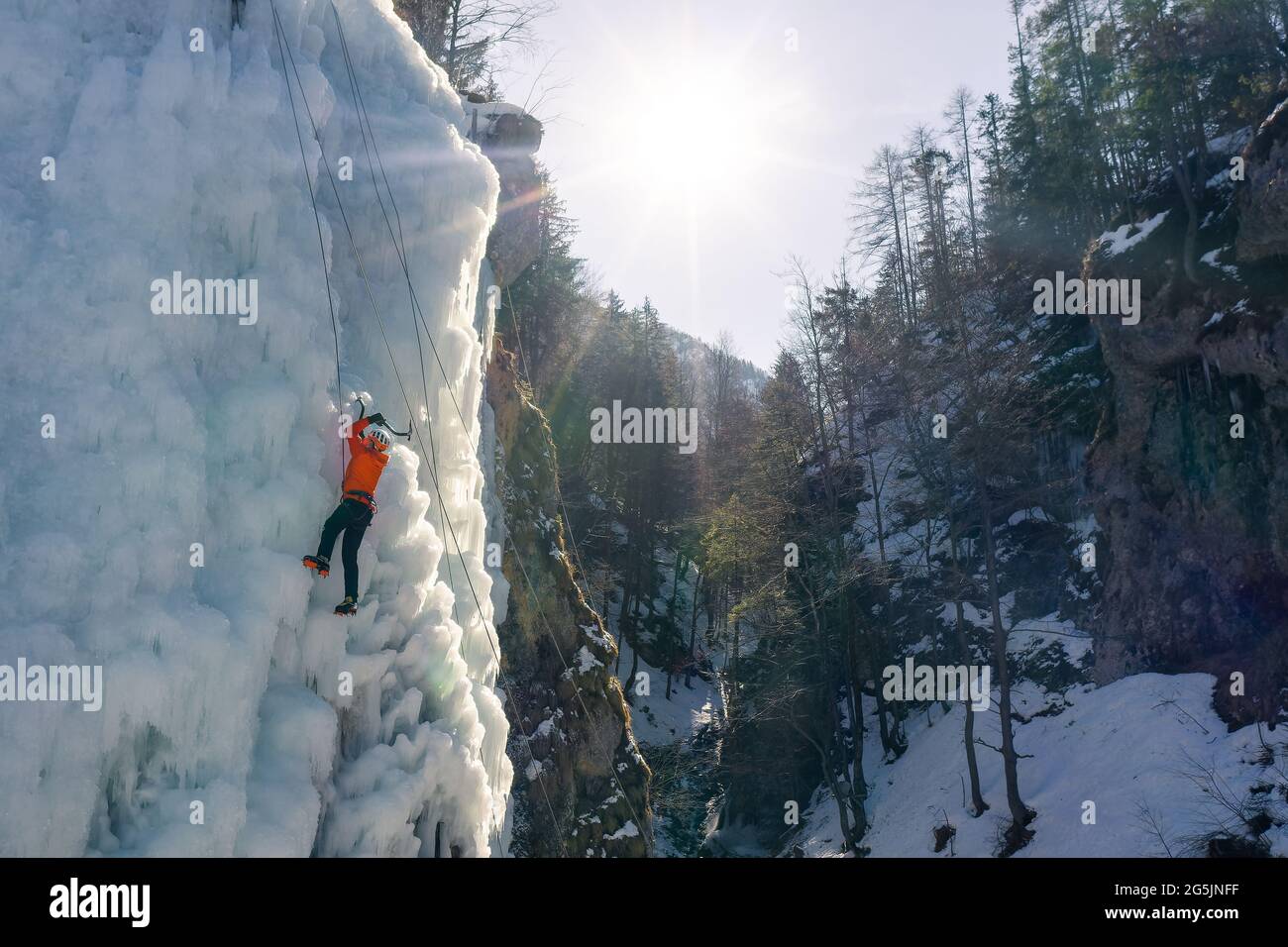 Mann klettert auf einem gefrorenen Wasserfall, indem er mit Steigeisen ins Eis tritt und auf das Eis drückt Stockfoto