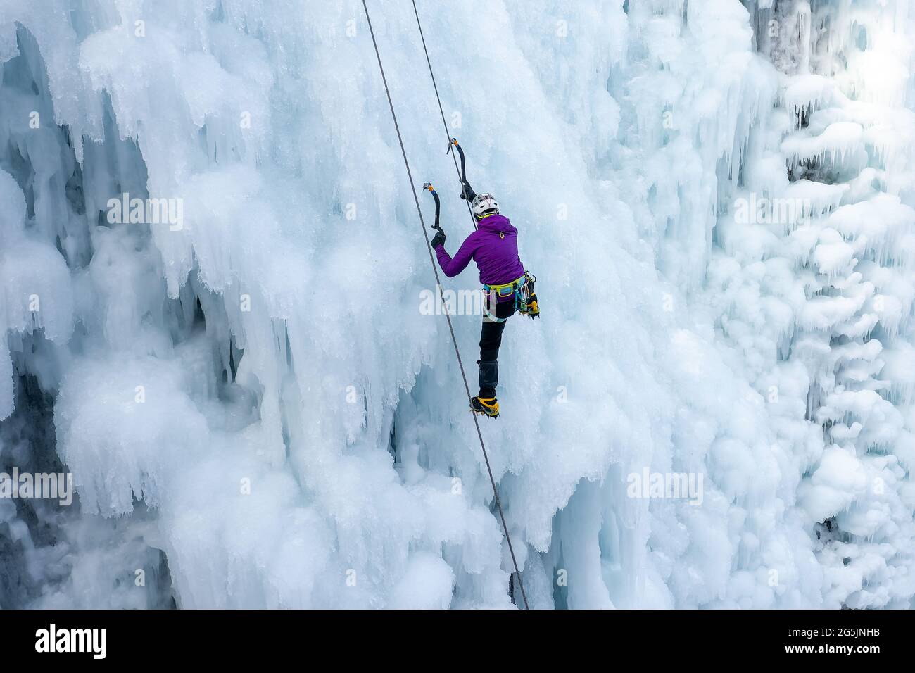 Eiskletterin klettert die Seite eines vereisten Hanges mit Unebenheiten, Graten und Eiszapfen hinauf Stockfoto