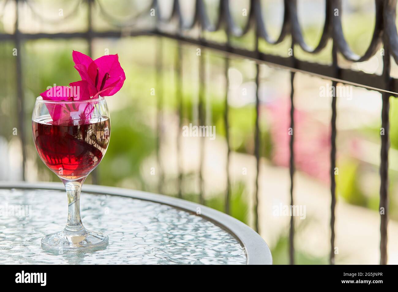 Romantischer Blick auf die Terrasse: Elegantes Glas Rotwein und dekorative rosa Blumen von Bougainvillea in einem Glas. Festliches Weihnachtskonzept. Speicherplatz kopieren. Stockfoto