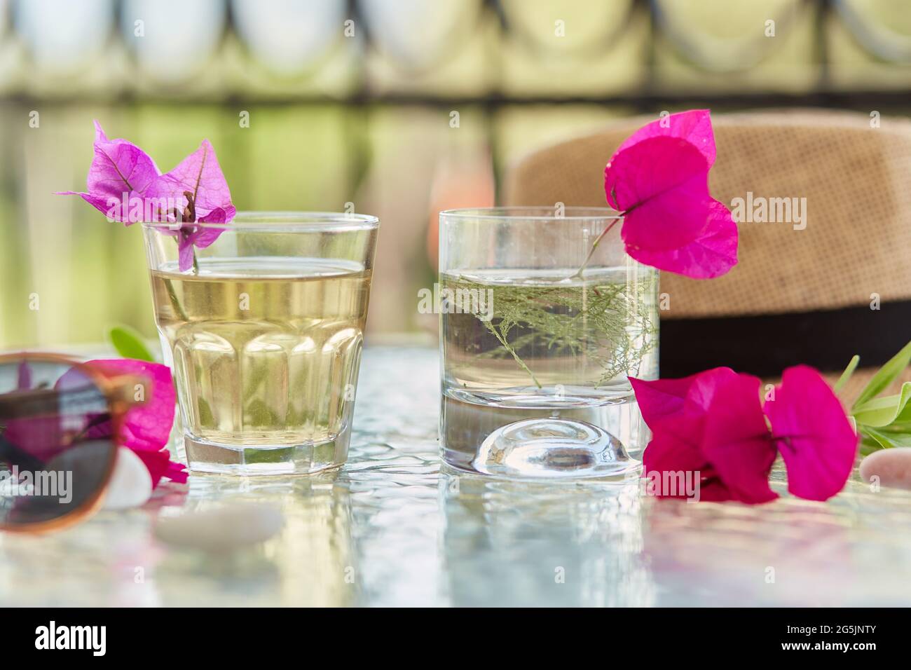 Helle Sommer hausgemachte Cocktails aus der Nähe und rosa Blüten von Bougainvillea Dekorationen mit Sonnencreme und Sommerhut. Sommertapete. Stockfoto