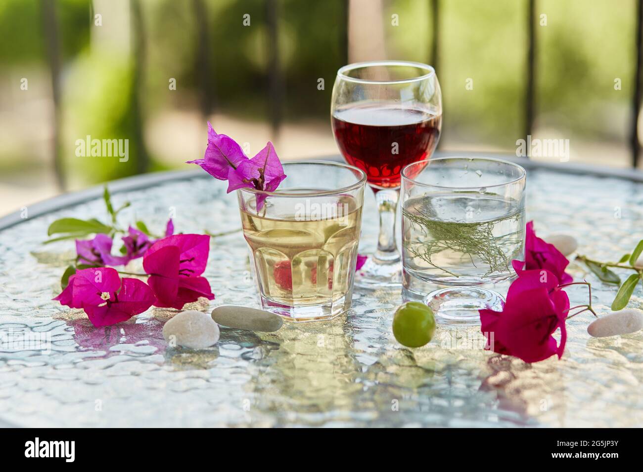 Im Sommer helle Cocktails und ein Glas Rotwein und rosa Blumen von Bougainvillea Dekorationen mit Kieselsteinen. Sommer Tapete aus nächster Nähe. Stockfoto