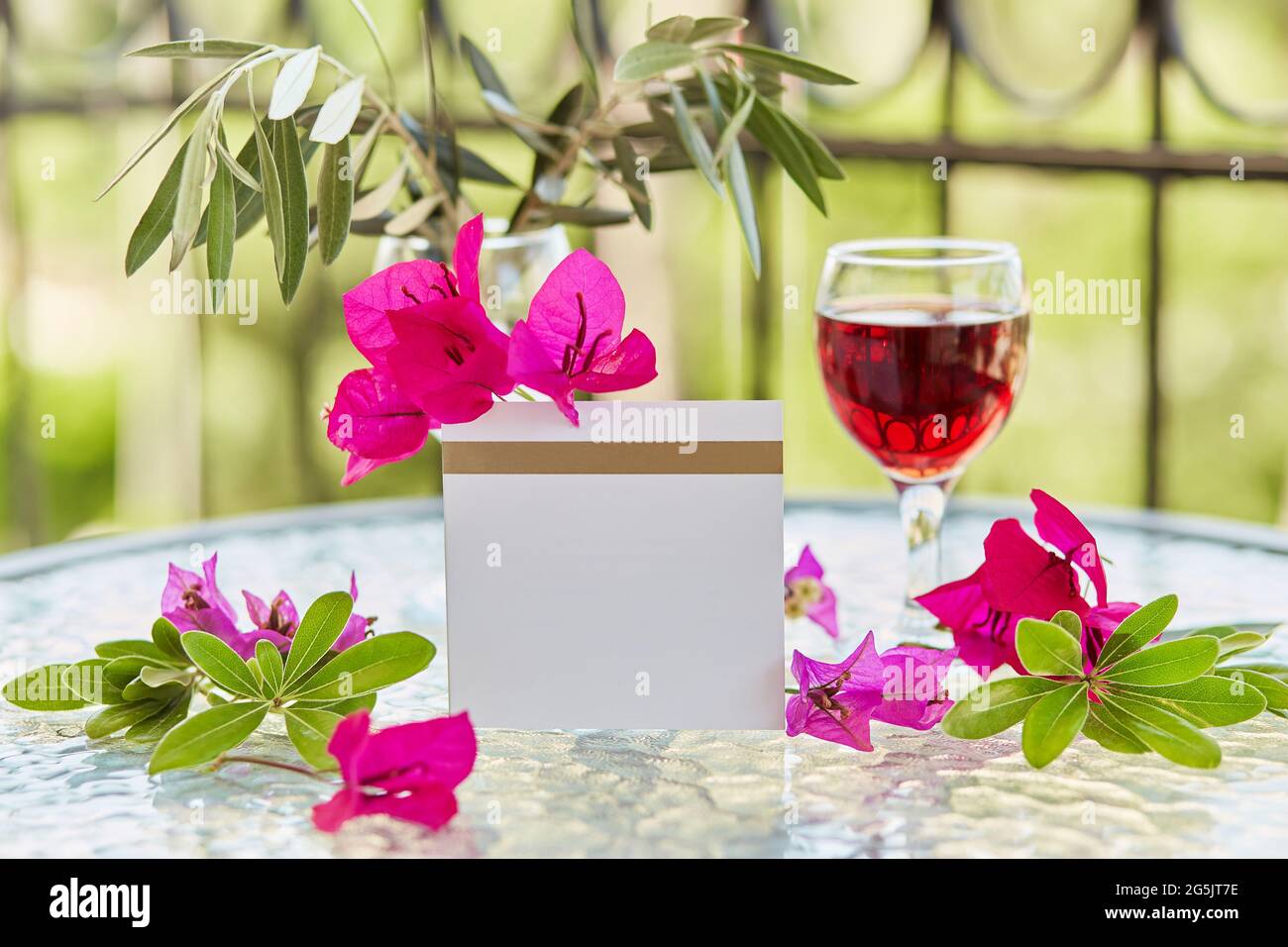 Nachbau einer Postkarte, Einladung. Elegantes Glas Rotwein. Dekorative rosa Blüten von Bougainvillea. Festliches, kreatives Urlaubskonzept. Dekorativer gre Stockfoto