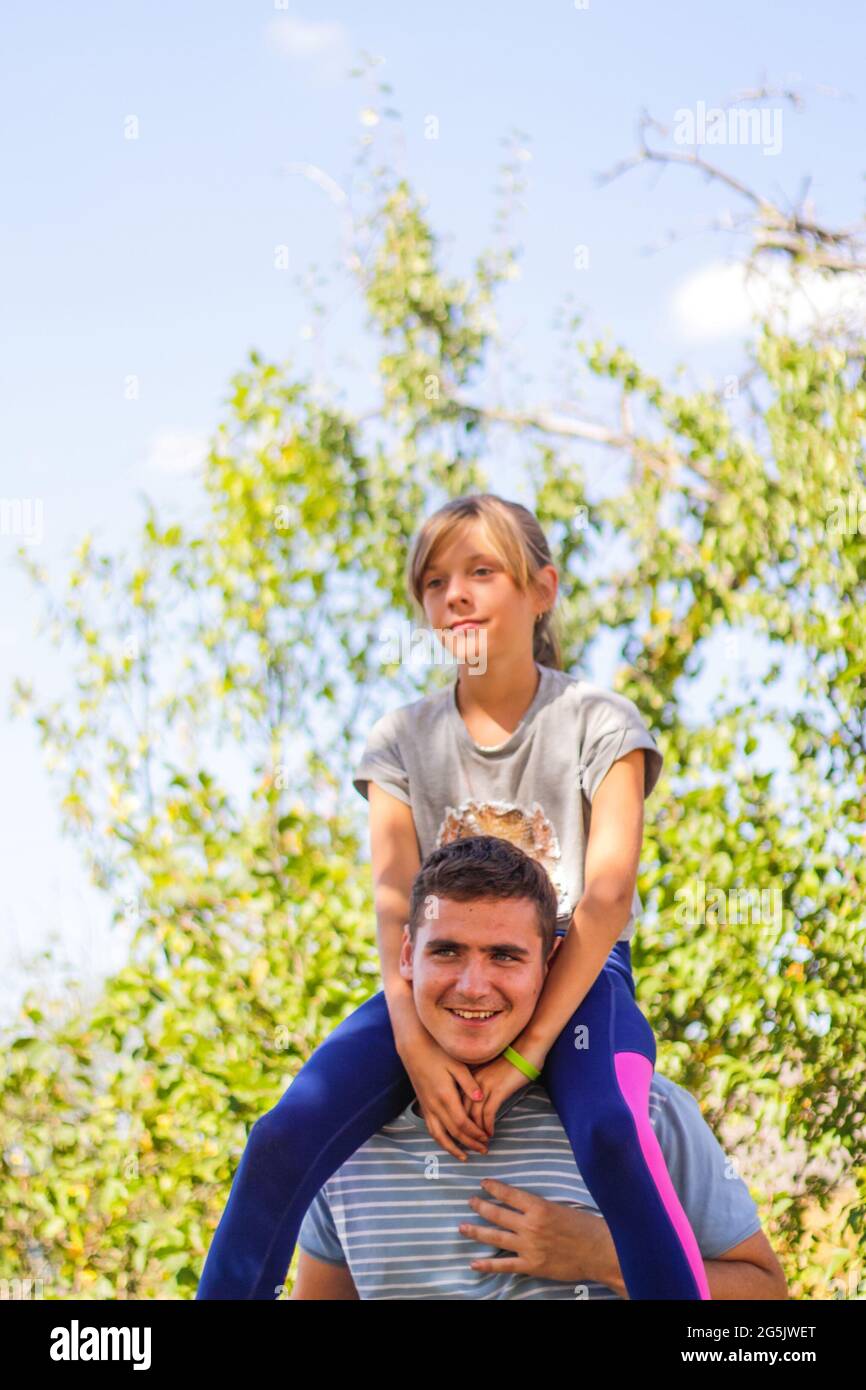 Defokussed Bruder geben Schwester Fahrt auf dem Rücken. Portrait von glücklichen Mädchen auf Mann Schultern, Huckepack. Familie spielt im Freien. Sommerferien lächelnd Stockfoto