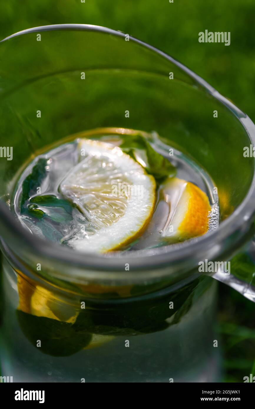 Unschärfe-Effekte aus der Nähe von Zitrone und Minze in einem Glaskrug mit Limonade auf natürlichem grünem Hintergrund. Krug mit kalten Sommercocktails oder Punsch im Freien, draußen Stockfoto
