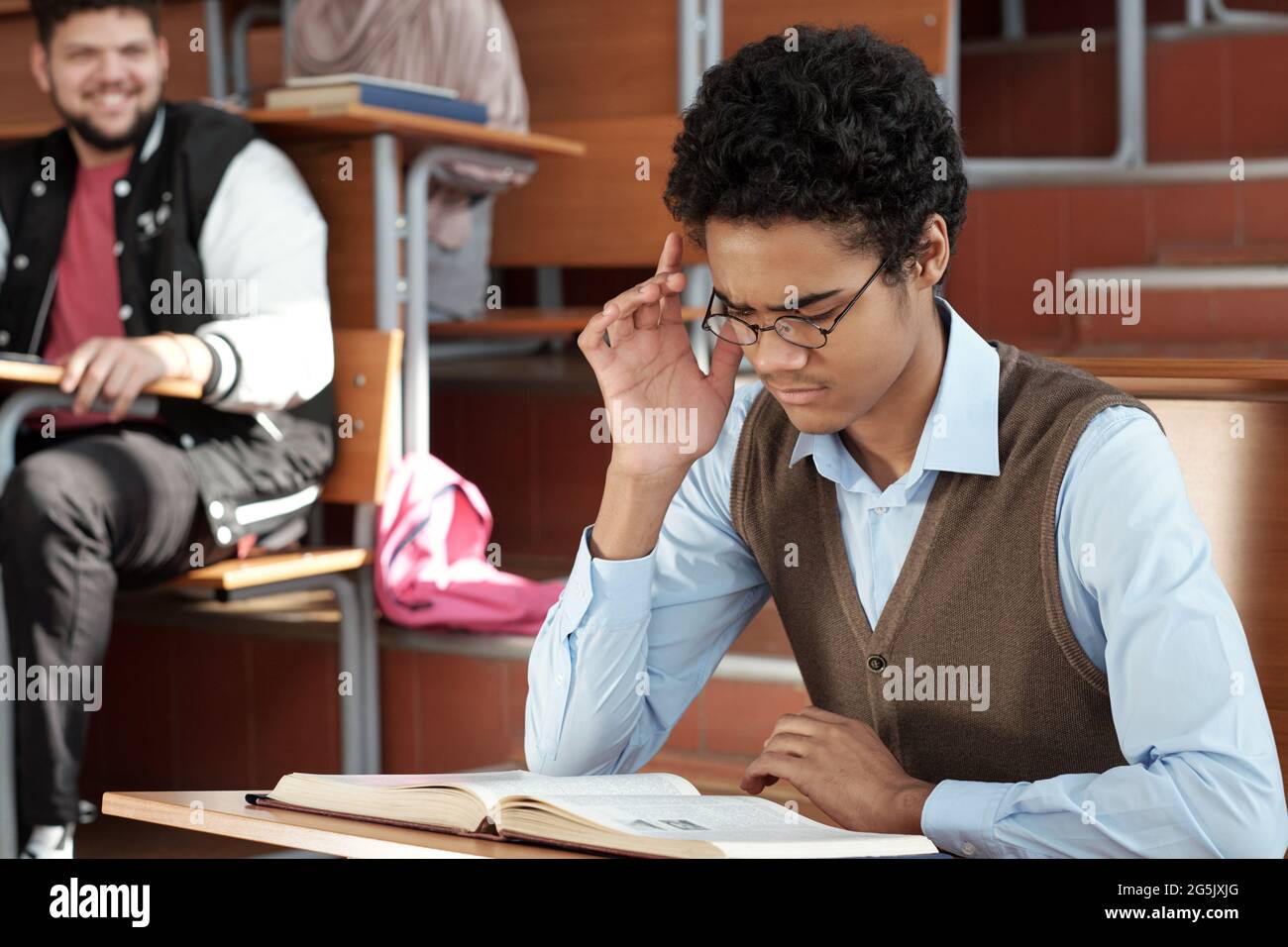 Gemischter Kerl, der versucht, sich beim Lesen des Buches in der Lektion zu konzentrieren Stockfoto