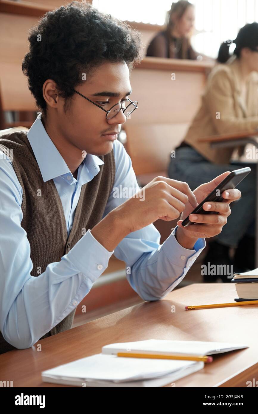 Gemischter Student scrollt während des Vortrags im Mobiltelefon Stockfoto