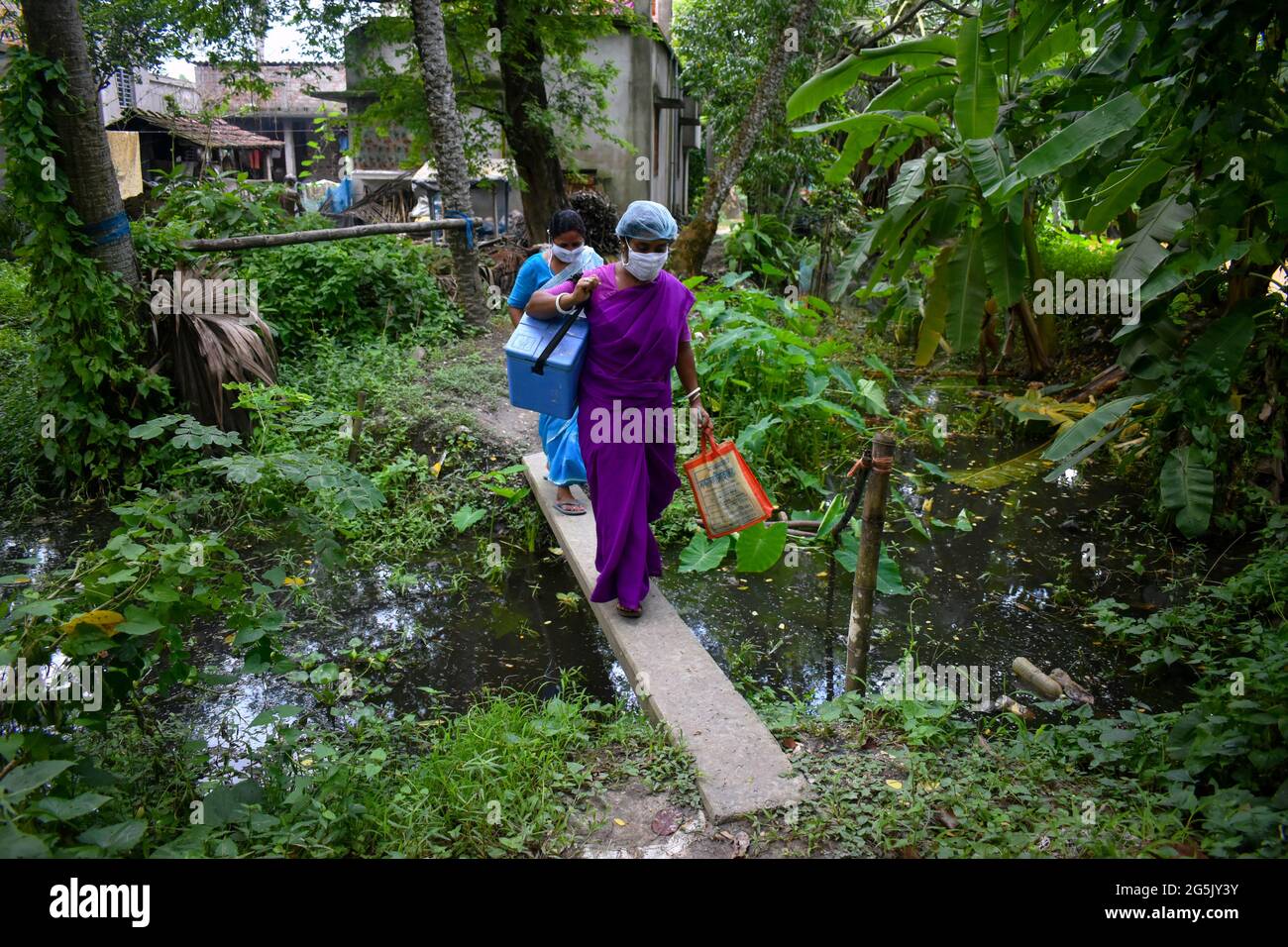 Kalkutta, Indien. Juni 2021. (6/27/2021) Kakali Mondal und Debrei Bagh, zwei Gesundheitshelfer, die einen Pulse-Polio-Impfstoff tragen und einen Pool überqueren, der von einem ungenutzten elektrischen Pfosten zur Tür-zu-Tür-Pulse-Polio-Impfung inmitten der anhaltenden COVID-19-Pandemie in Dakshin Bonhooghly, South 24 Parganas, Westbengalen, hergestellt wurde. (Foto: Sudipta das/Pacific Press/Sipa USA) Quelle: SIPA USA/Alamy Live News Stockfoto