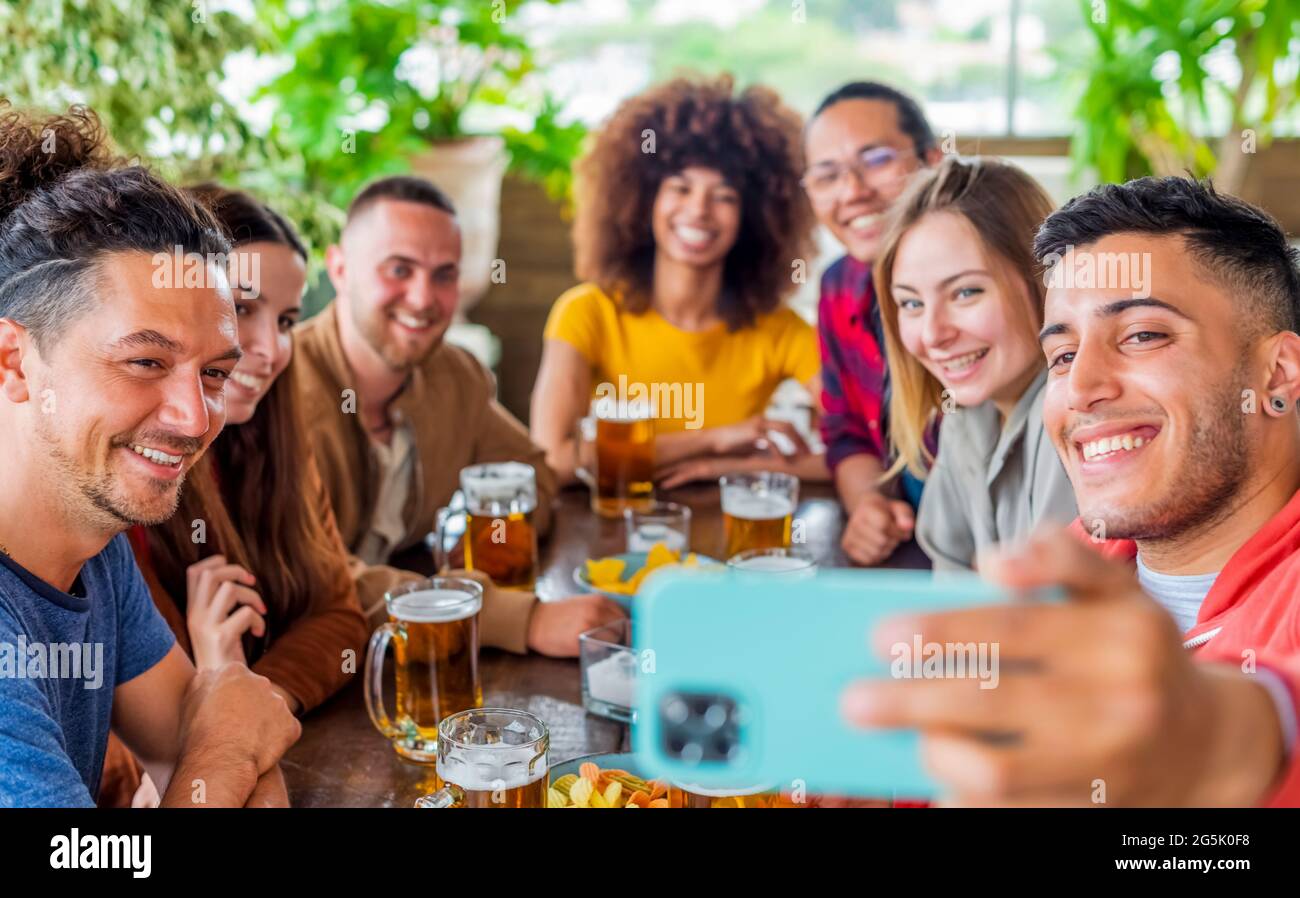 Diverse Freunde machen ein Selfie und feiern Happy Hour mit Bier und Essen in einem Bar-Restaurant. Multiethnische Menschen, die Spaß auf einer Party haben Stockfoto