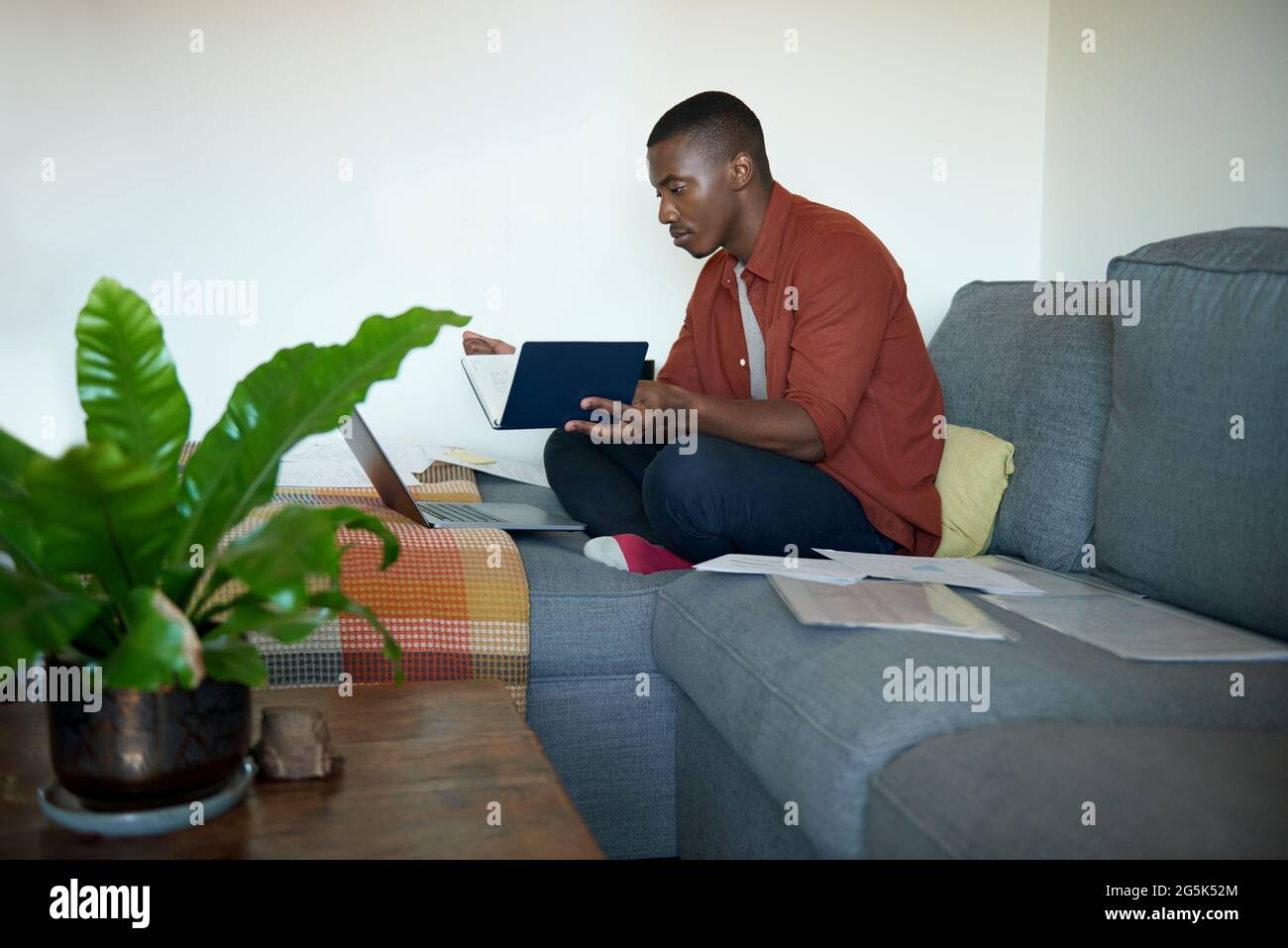 Junger afrikanischer Mann, der von zu Hause aus auf seinem Sofa im Wohnzimmer arbeitet Stockfoto