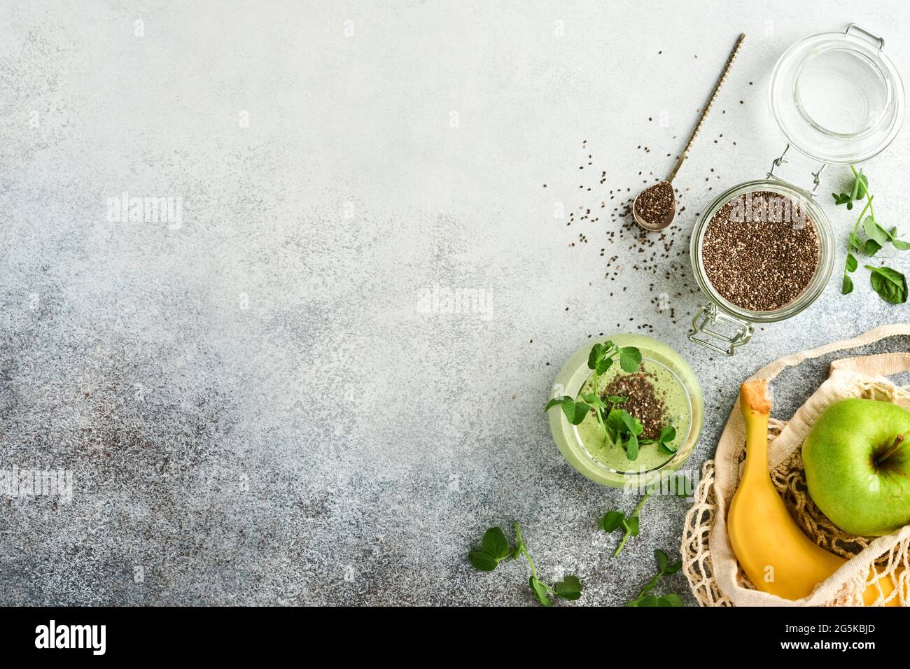 Ein Glas gesunden grünen Smoothie und Zutaten für Smoothie, frischen Spinat, Chiasamen, Erbsen-Mikrogemüse, Banane, Kiwi und Apfel im wiederverwendbaren Einkauf b Stockfoto