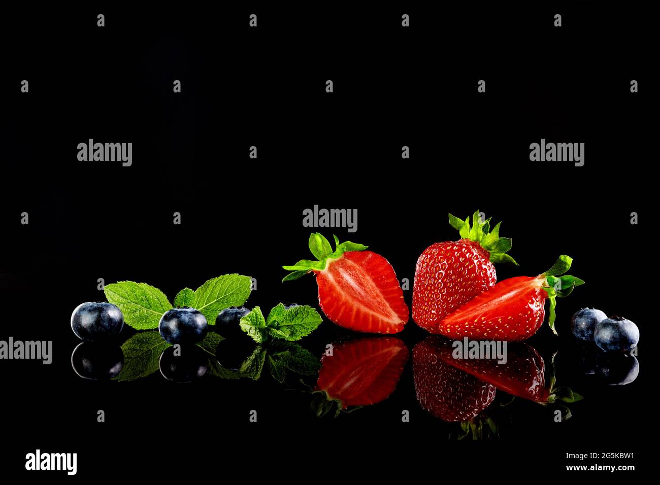 Erdbeeren und Heidelbeeren mit Minzblättern auf dem schwarzen Glashintergrund mit einer Spiegelung. Selektiver Fokus. Stockfoto