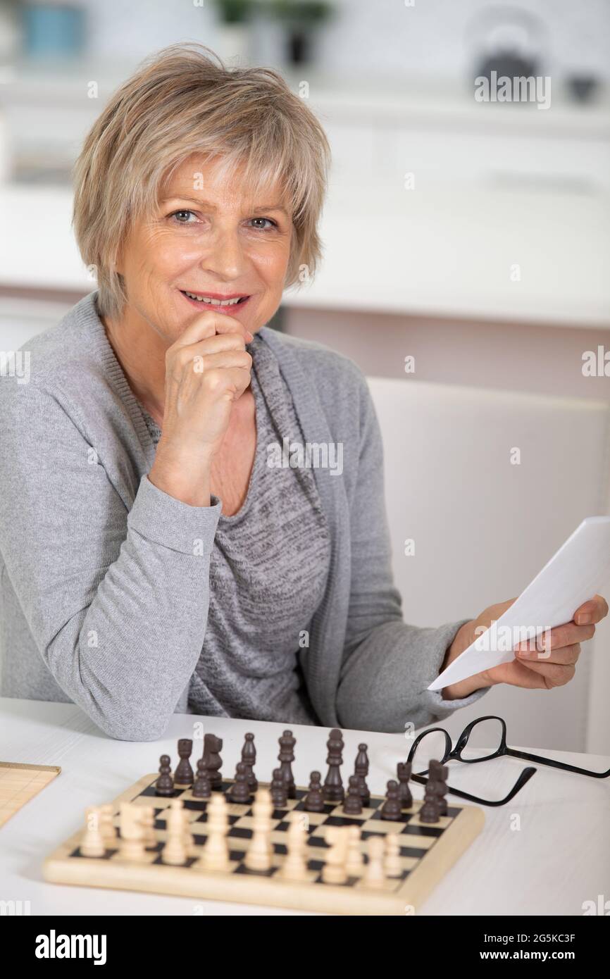 Ältere Frau denkt in Innenräumen über eine Schachkombination nach Stockfoto