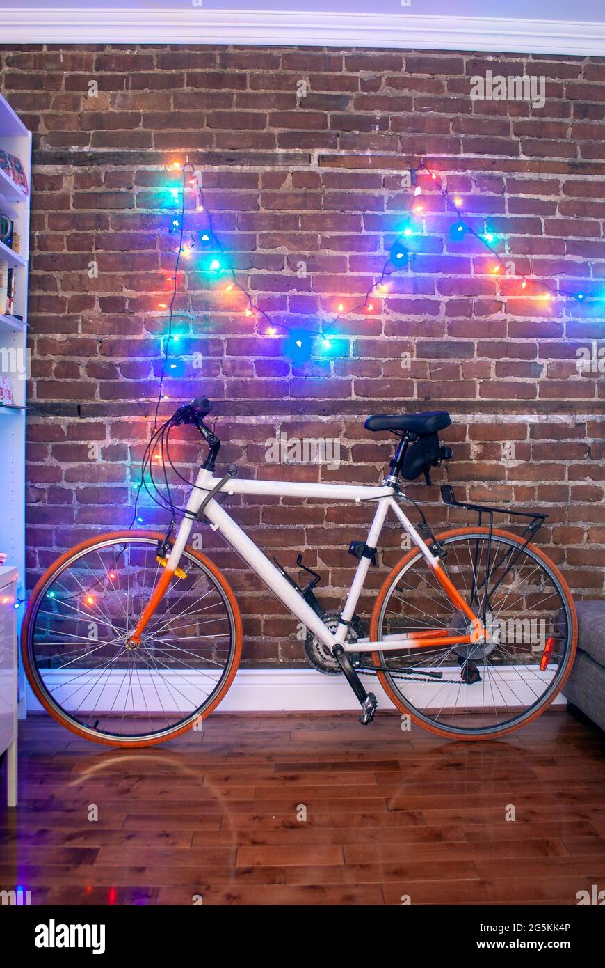 Farbenfrohes Fahrrad, das sich an der Ziegelwand eines Raumes lehnt, mit Weihnachtslichtern, die an der Wand entlang aufgereiht sind Stockfoto