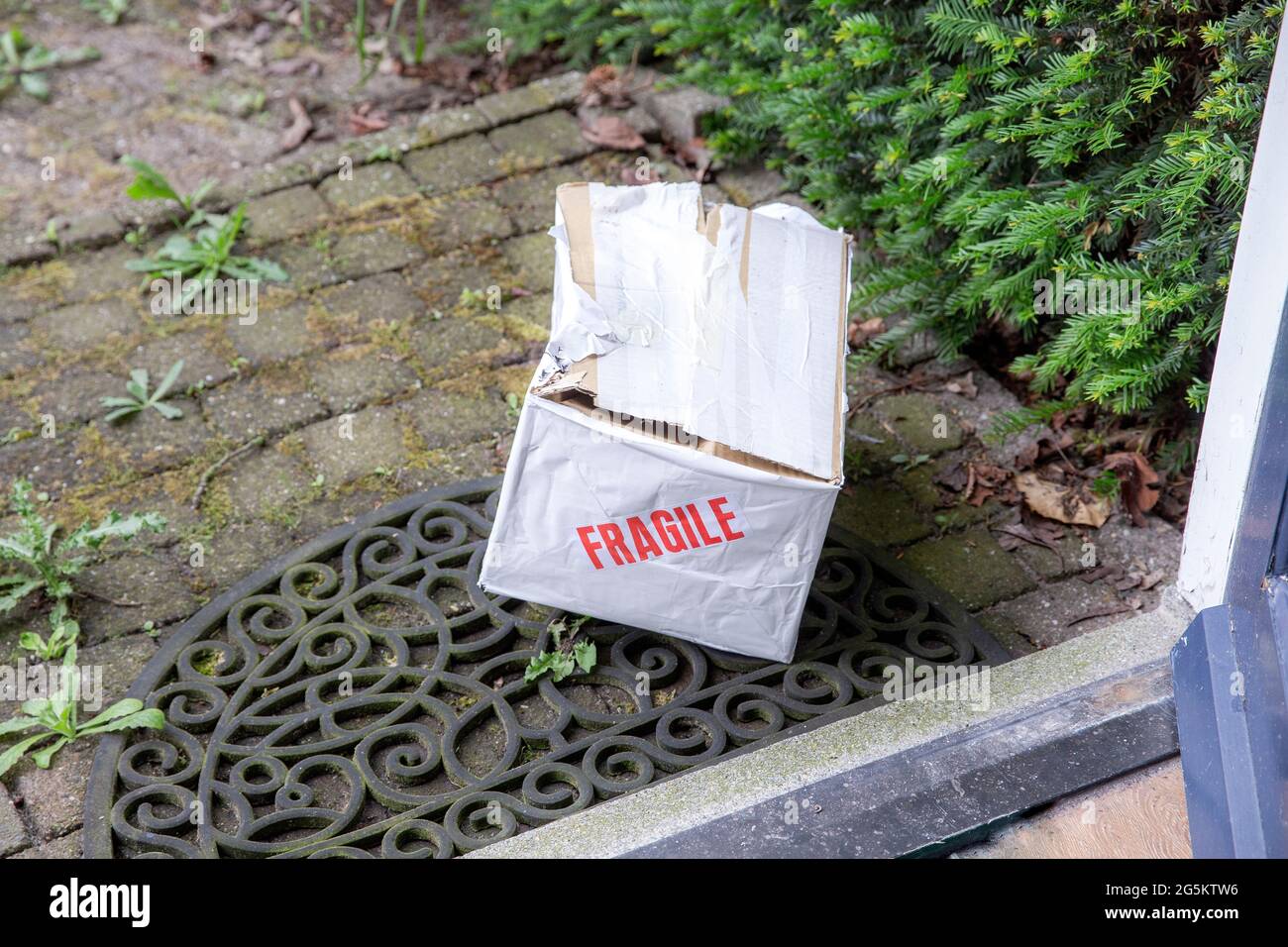 Beschädigter Lieferkarton an der Haustür eines Hauses, zerbrechliches Paket mit Beulen, schlechtes Lieferkonzept Stockfoto