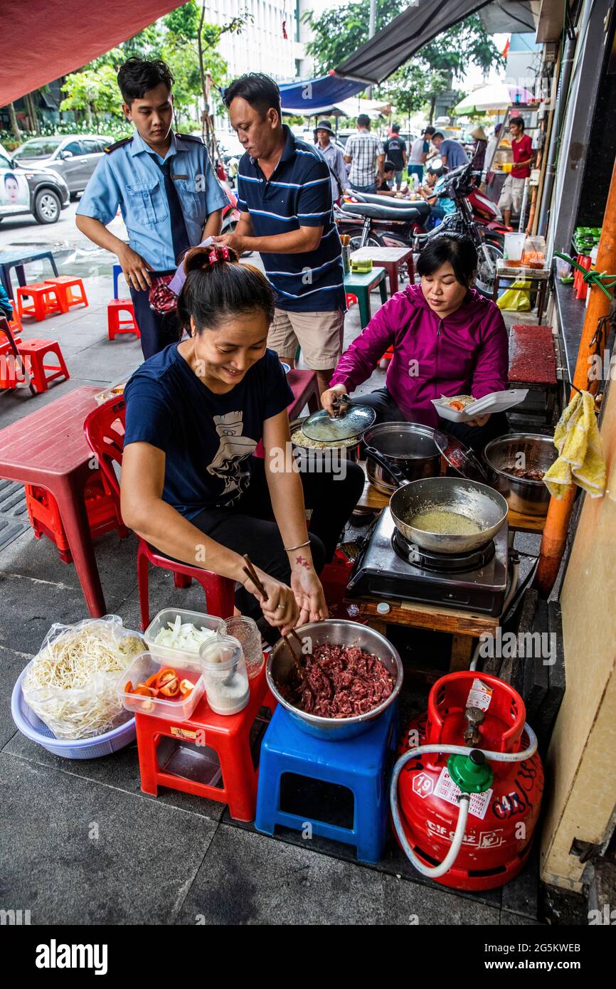 Frauen kochen Lunch Street Food Vorspeisen, während zwei Männer auf ihre Mahlzeiten warten Stockfoto