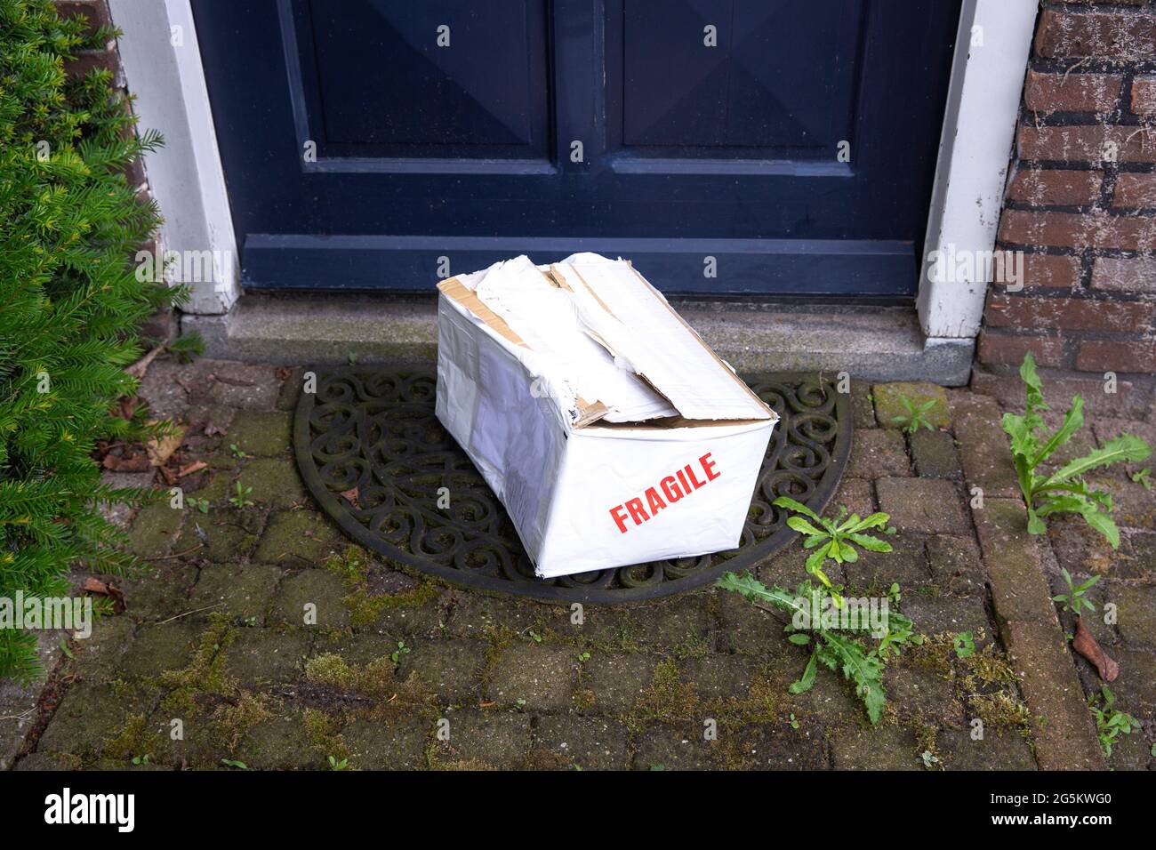 Beschädigter Lieferkarton an der Haustür eines Hauses, zerbrechliches Paket mit Beulen, schlechtes Lieferkonzept Stockfoto