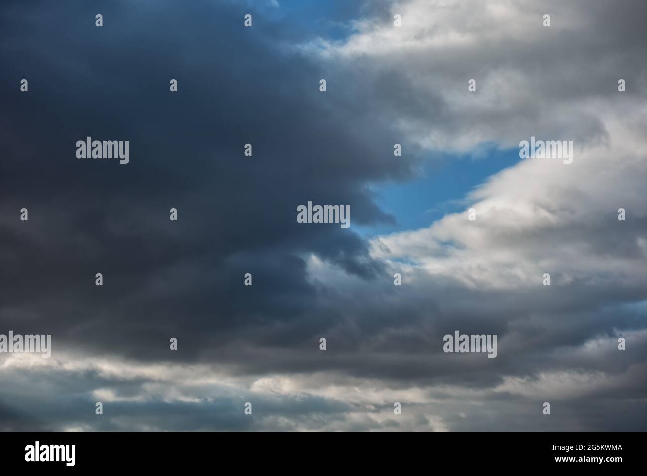 Himmelshintergrund mit schweren dunkelgrauen, fast schwarzen stürmischen Wolken von einer Seite und kontrastierenden weißen Wolken von einer anderen Seite. Blauer Himmel ist sichtbar Stockfoto
