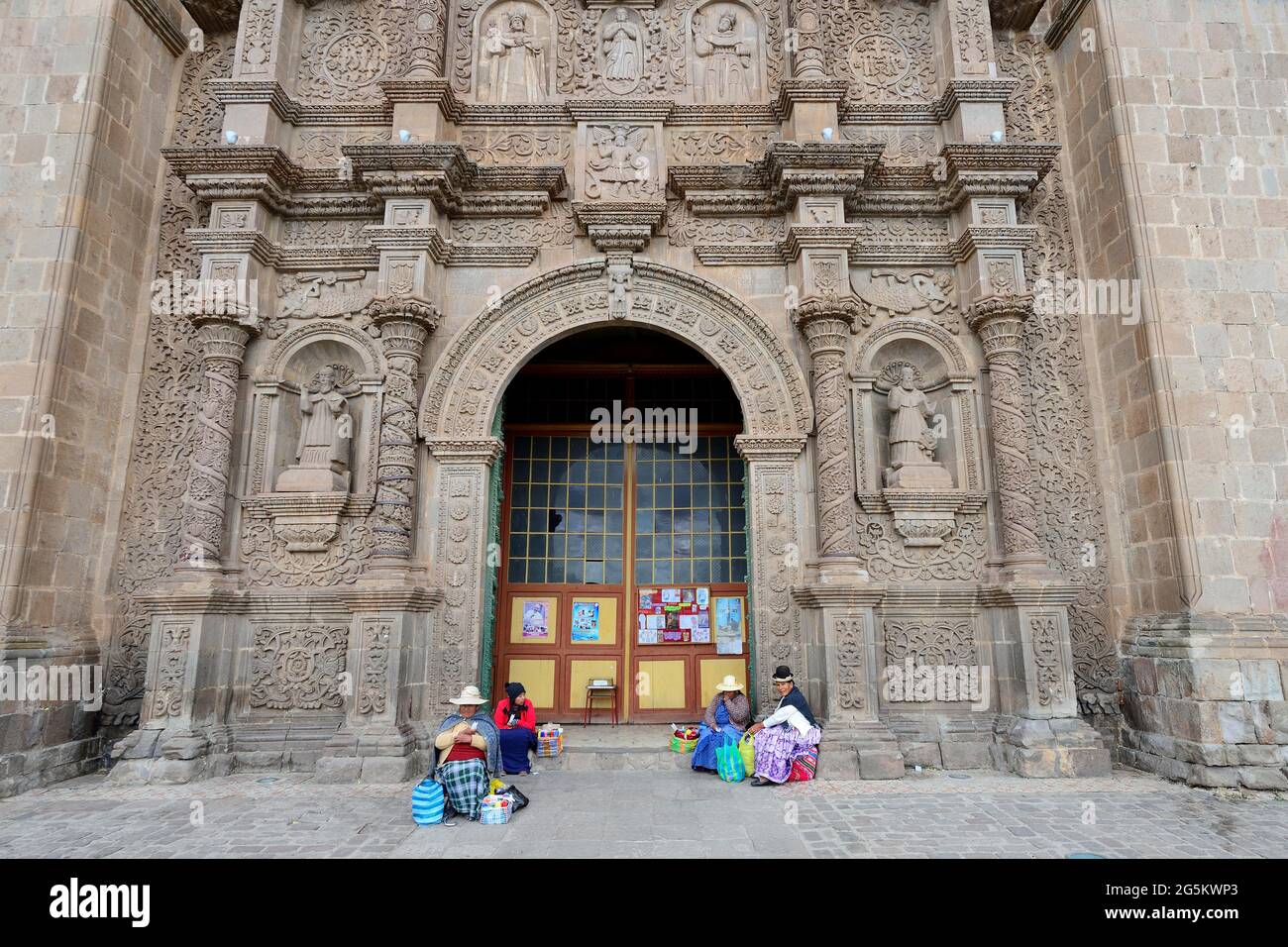 Indigene Frau in traditioneller Tracht sitzt vor dem Tor der Kathedrale, Catedral Basílica San Carlos Borromeo, Puno, Lake Titicaca, per Stockfoto