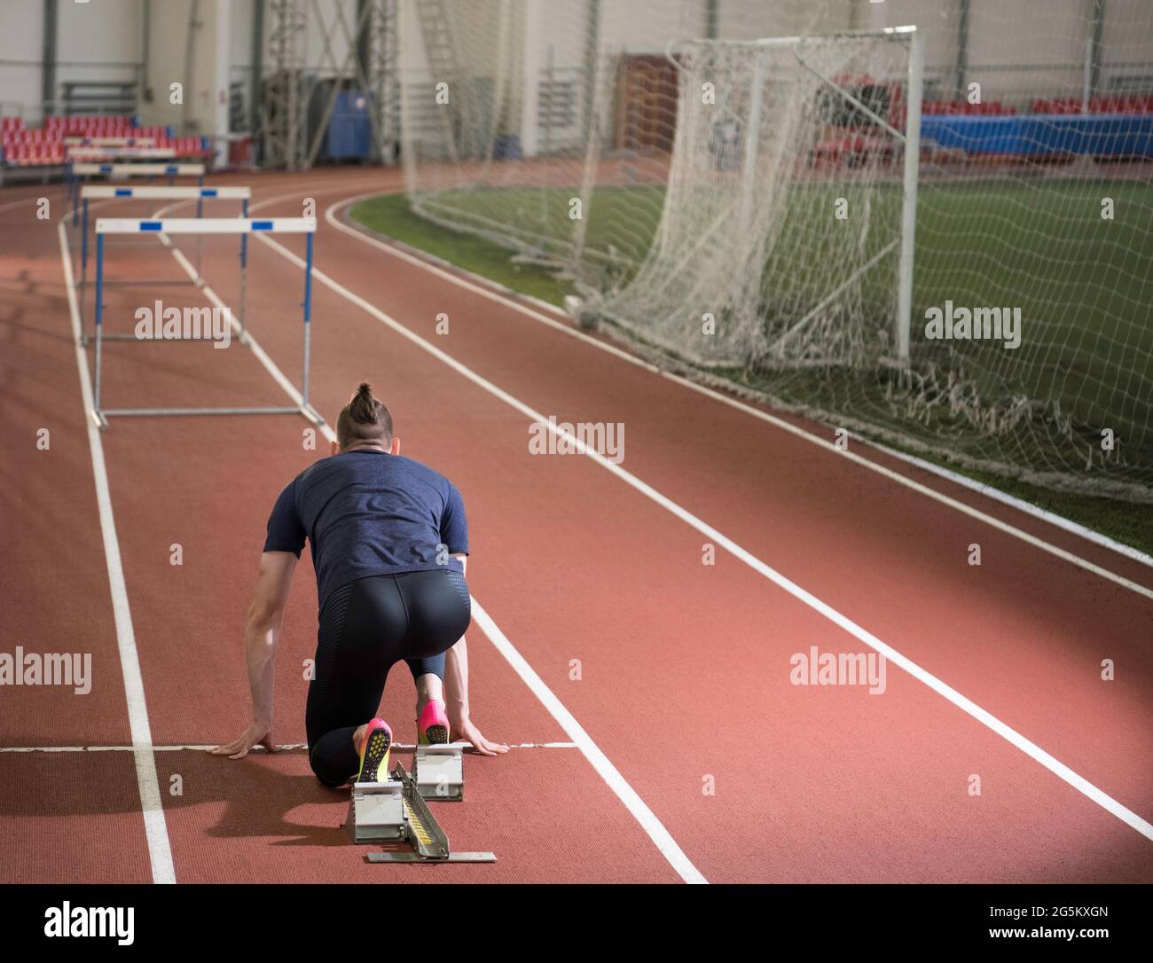 Männlicher Athlet, der sich auf Blockaden vorbereitet, um von der Startposition des Crouchers aus einen Barrierelauf zu machen Stockfoto