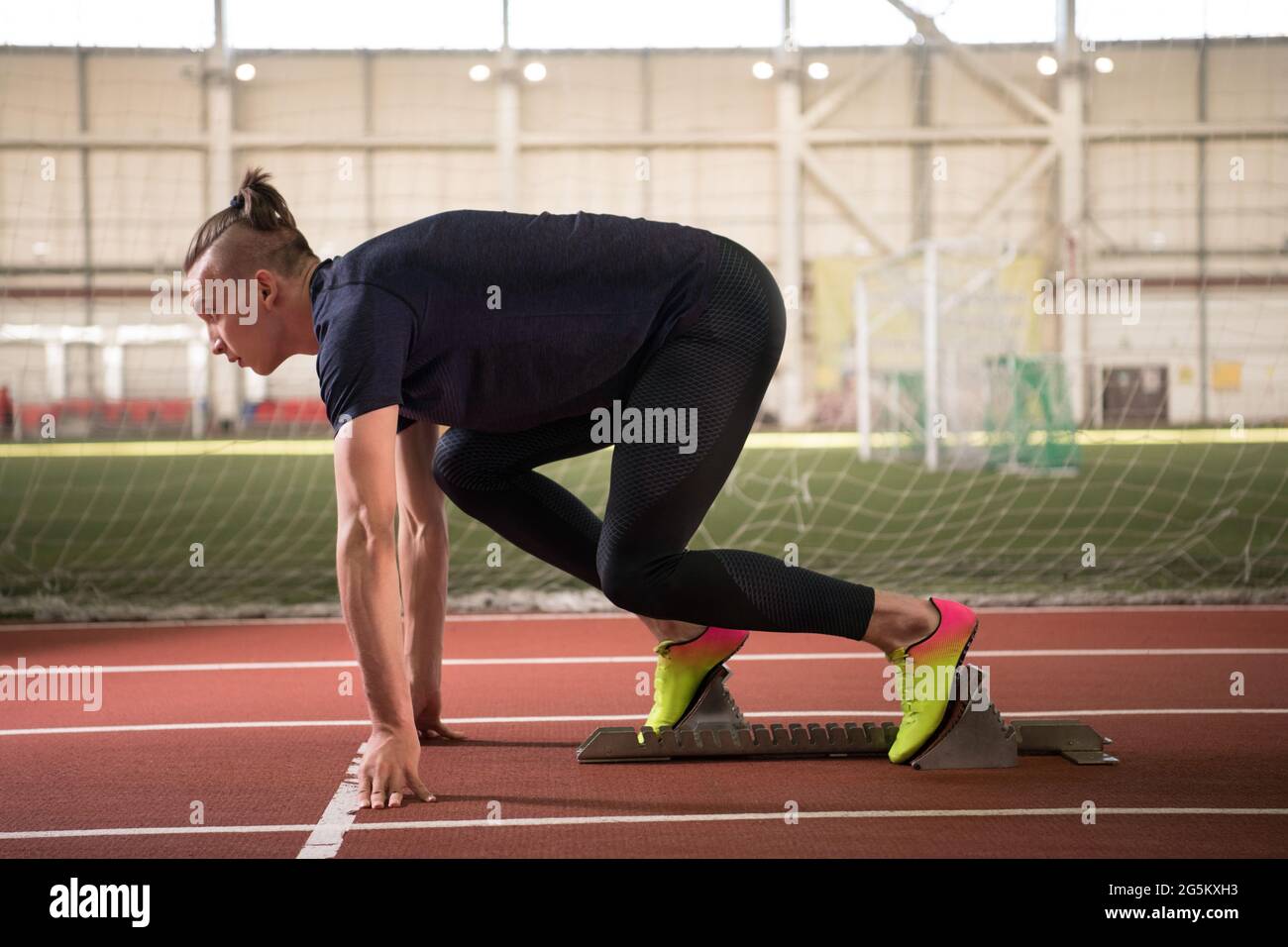 Fokussierter Sportler, der in der Crouch-Startposition auf Blöcken steht und sich auf den Lauf vorbereitet Stockfoto