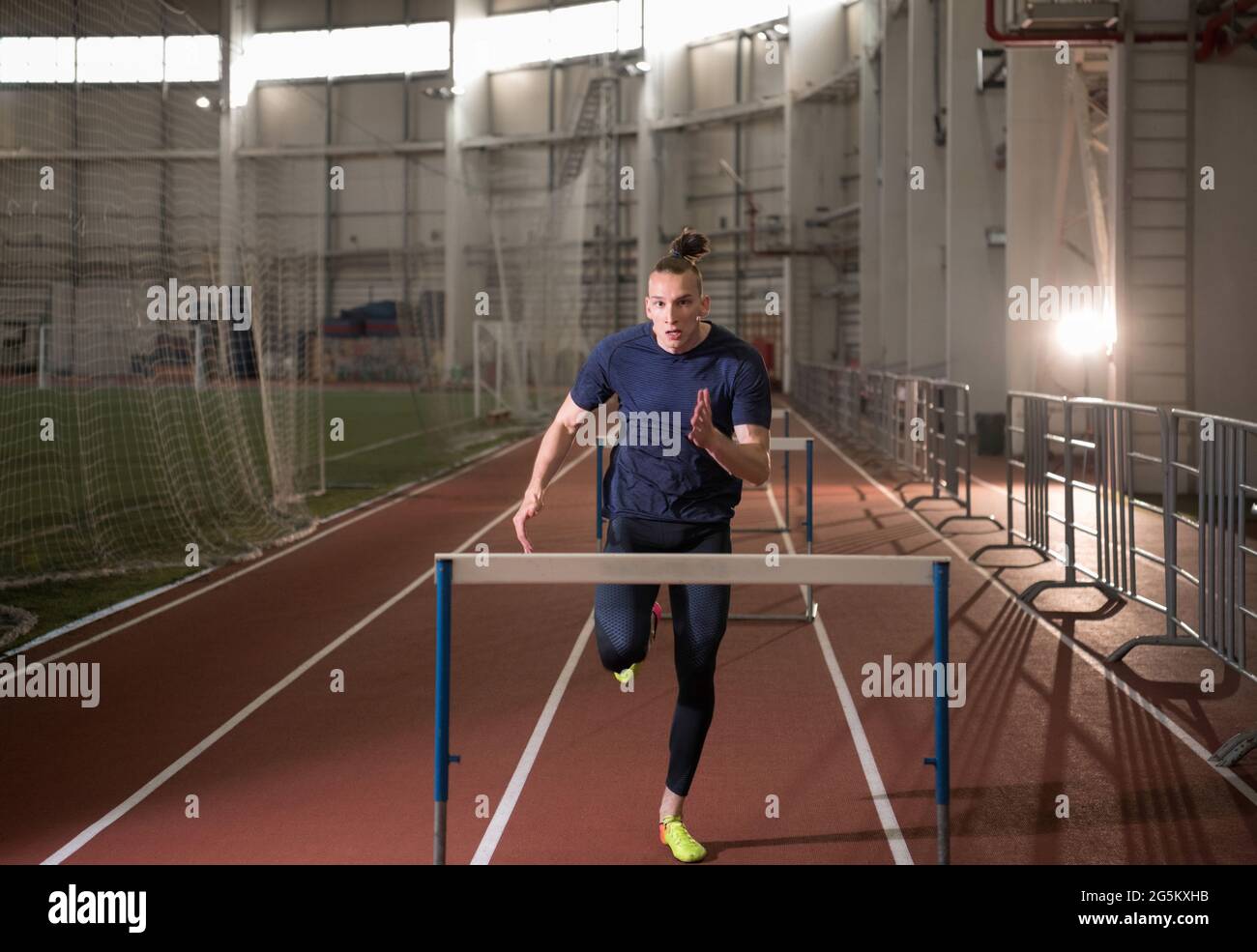 Junger männlicher Athlet beim Laufen und Hürden beim Leichtathletik-Training im Stadion Stockfoto