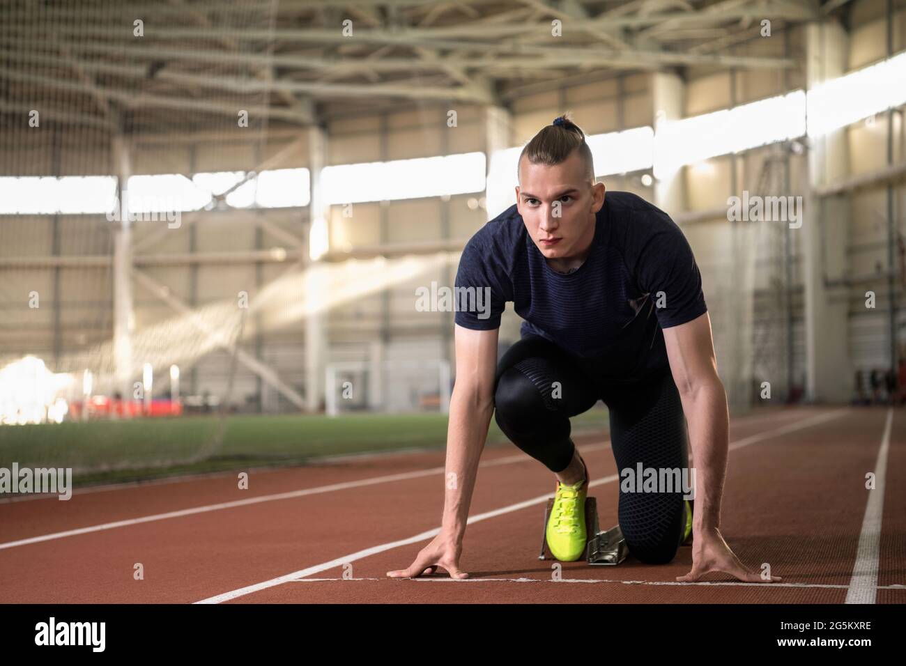 Fokussierter männlicher Athlet, der sich darauf vorbereitet, von der Startposition der Crouch-Mannschaft auf der Strecke im Stadion zu laufen Stockfoto