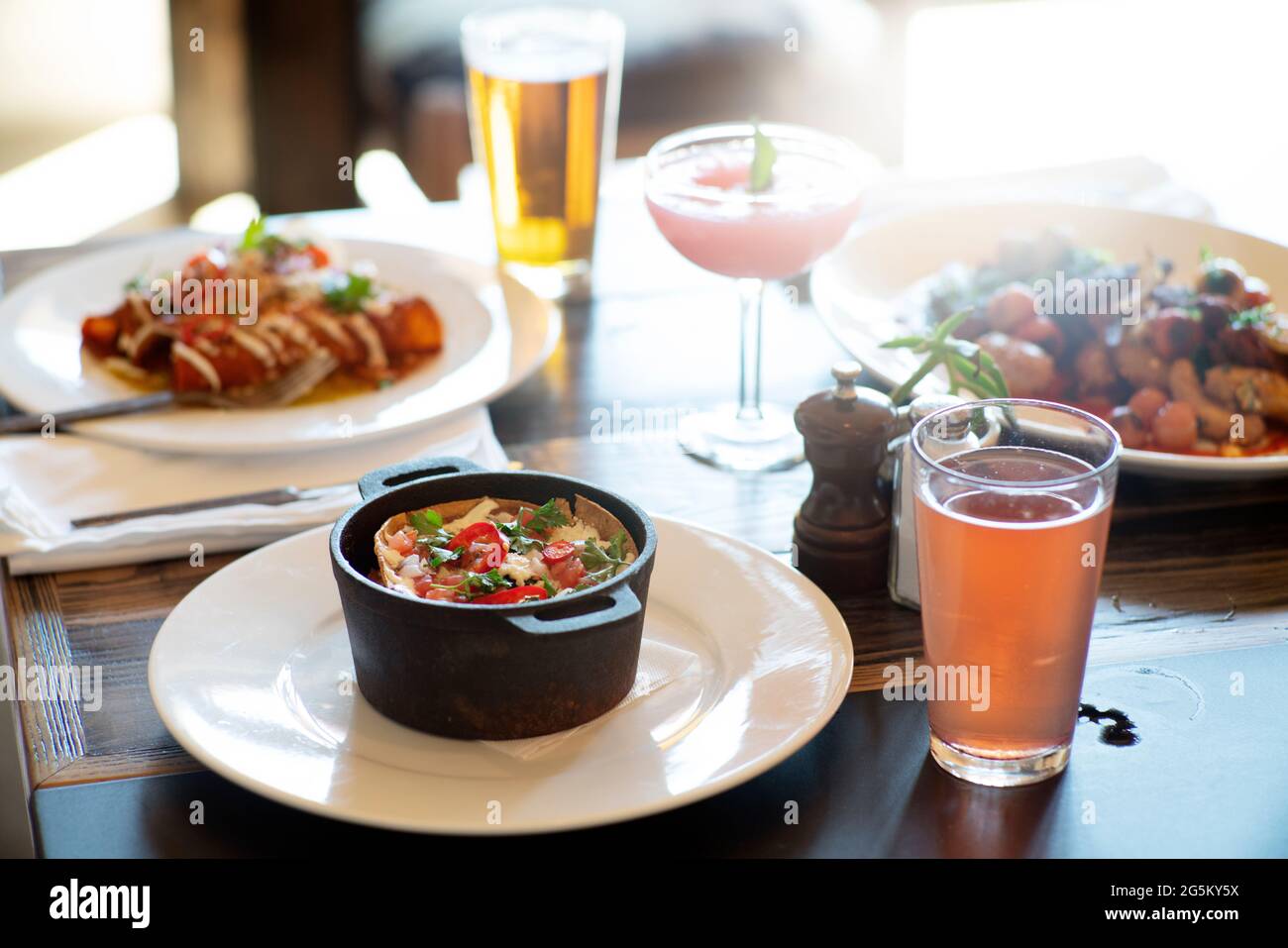 Hauptgerichte und Getränke auf einem Tisch in einem Restaurant mit Hintergrundbeleuchtung und Lichtreflexen. Stockfoto