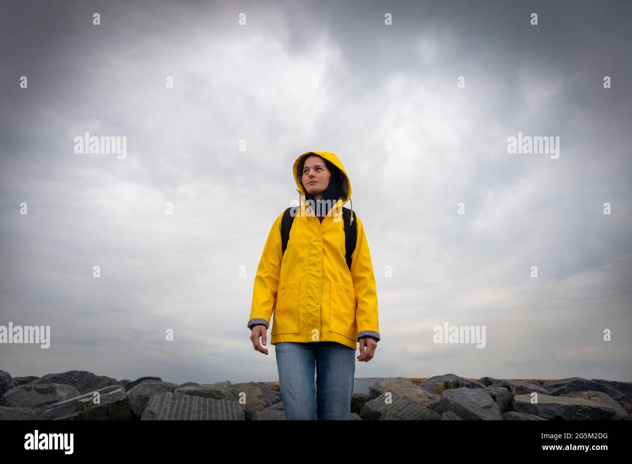 Wandererin mit gelbem Mantel, die bei schlechtem Wetter auf Felsen steht. Stockfoto