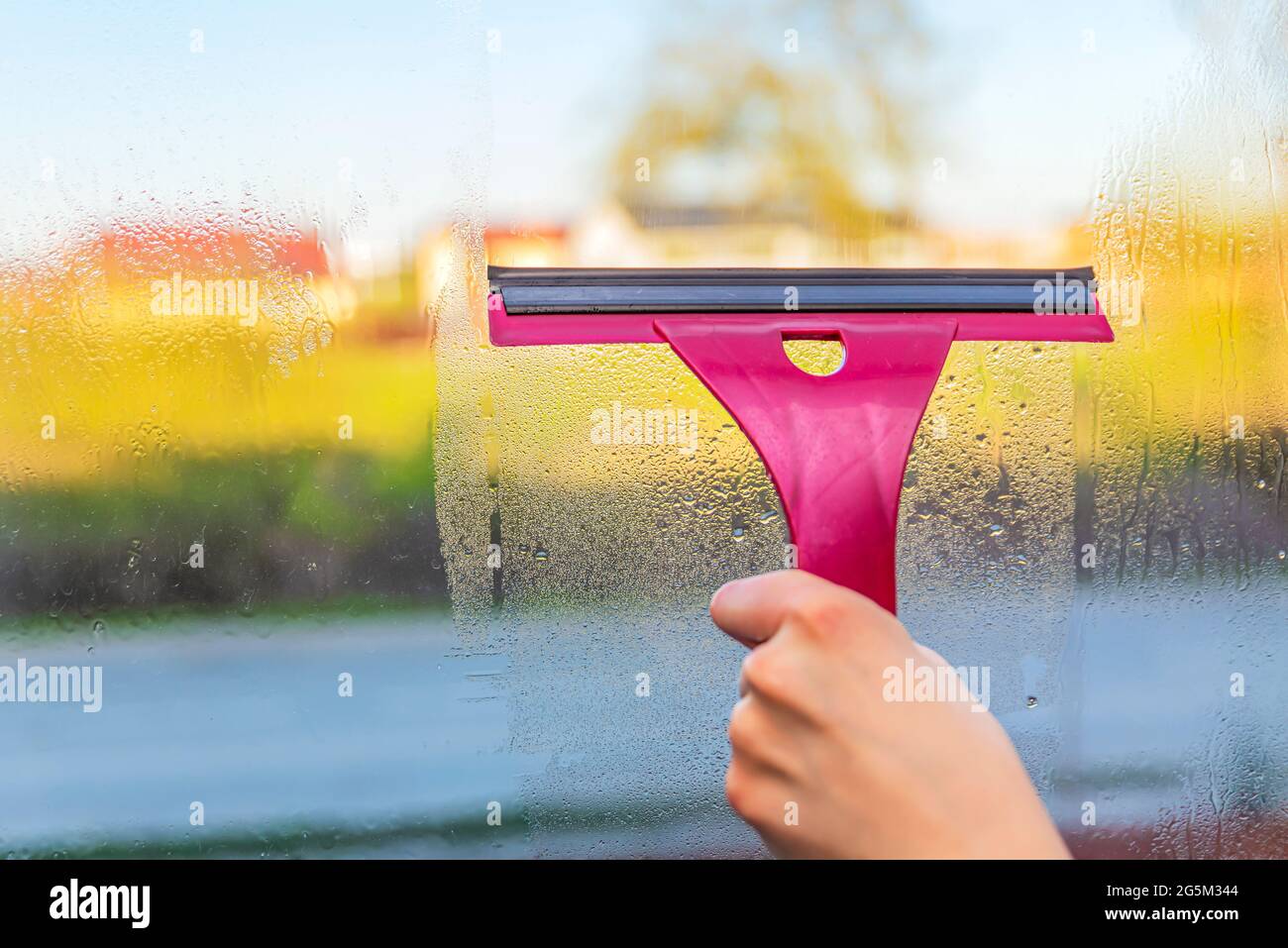 Kondenswasser tropft auf das Fenster. Frau entfernt Kondenswasser aus Fensterscheiben. Kalte Jahreszeit. Temperaturdifferenz. Stockfoto