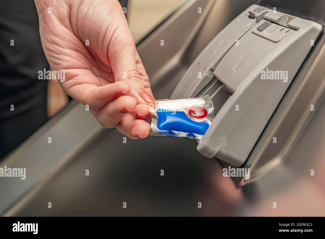 Spülmaschinenkapsel, legt die Frau die Kapsel in den Geschirrspüler, bevor sie die Pasta wäscht Stockfoto