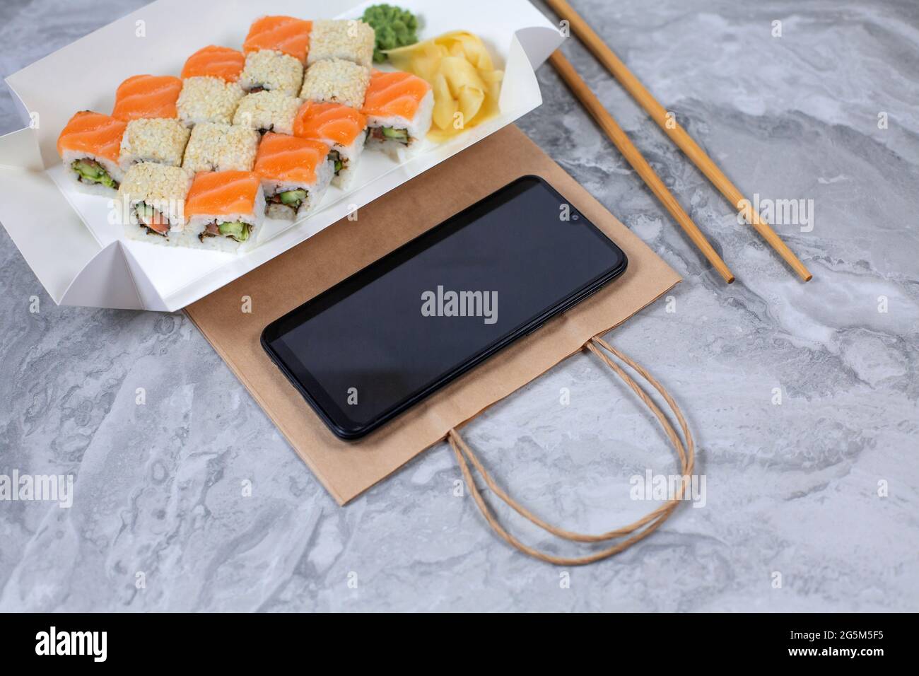 Leckere Sushi-Brötchen und Smartphone auf Steintisch, Draufsicht. Lieferung von Lebensmitteln. Sushi-to-go-Konzept. Stockfoto