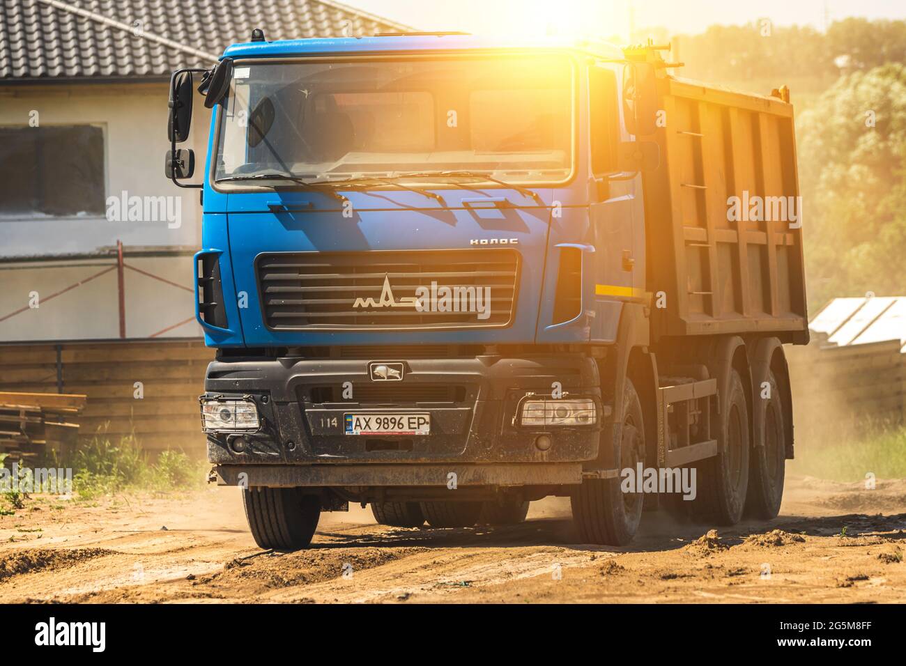 Charkow, Ukraine - 22. Juni 2021: Blauer Kipper bei Sonnenuntergang auf der Baustelle bewegt sich in Staub und Schmutz, schwere Maschinenaufnahme Stockfoto