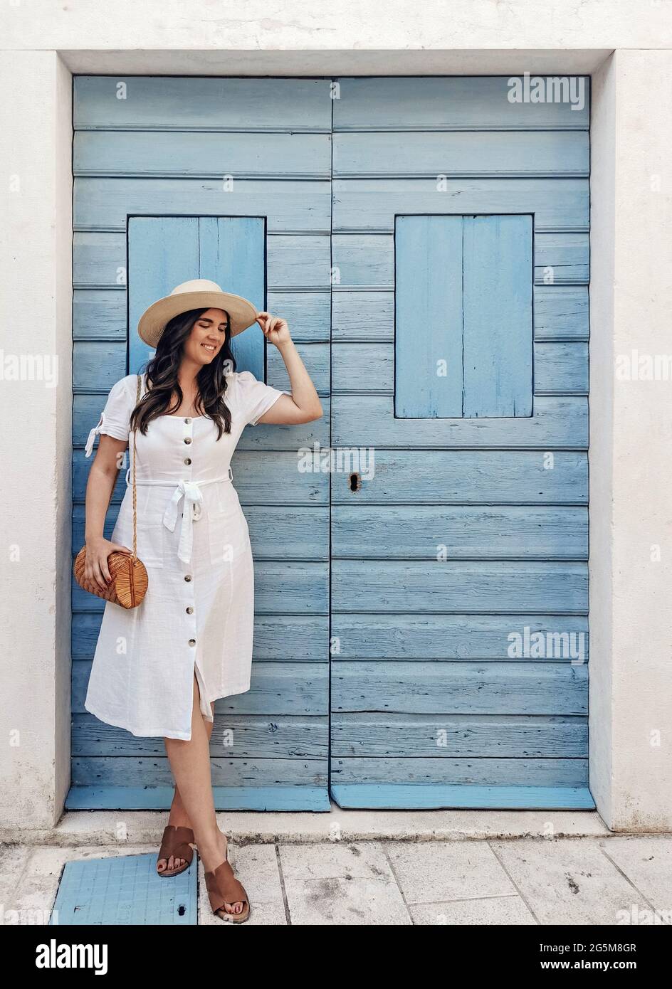 Vorderansicht Ganzkörperporträt der lächelnden jungen Frau, die vor der pastellblauen Holztür steht Stockfoto