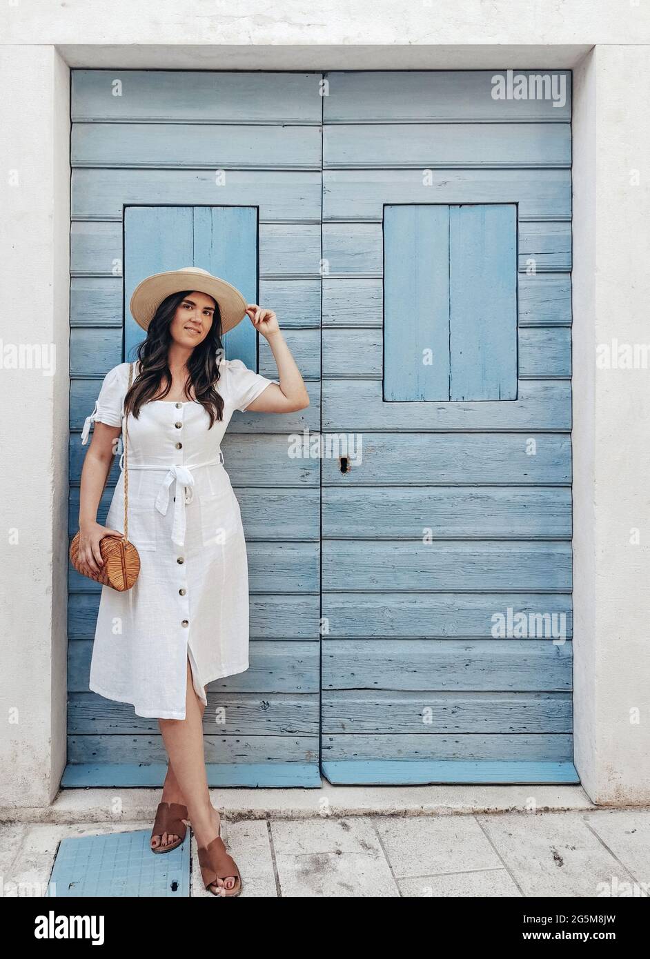 Vorderansicht Ganzkörperporträt der lächelnden jungen Frau, die vor der pastellblauen Holztür steht Stockfoto
