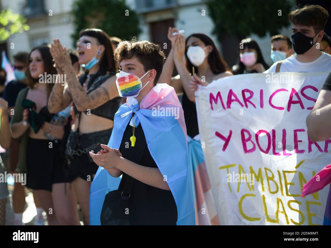 Ein Protestler, der eine Gesichtsmaske trägt und mit einer Flagge gewickelt ist, sieht er applaudieren, als er an einem Protest zur Feier des Internationalen LGTBI Pride Day auf dem Plaza de la Merced teilnimmt. Dutzende von Menschen haben sich in der Innenstadt versammelt, um an der „kritischen Stolz“ gegen Homophobie und Transphobie sowie zur Unterstützung der geschlechterspezifischen Selbstbestimmung von Transgender-Menschen teilzunehmen. Schwule, Lesben, Bisexuelle und Transsexuelle gedenken jeden 28. Juni der Demonstrationen von Stonewall für die Rechte der LGTBI-Gemeinschaft. Stockfoto