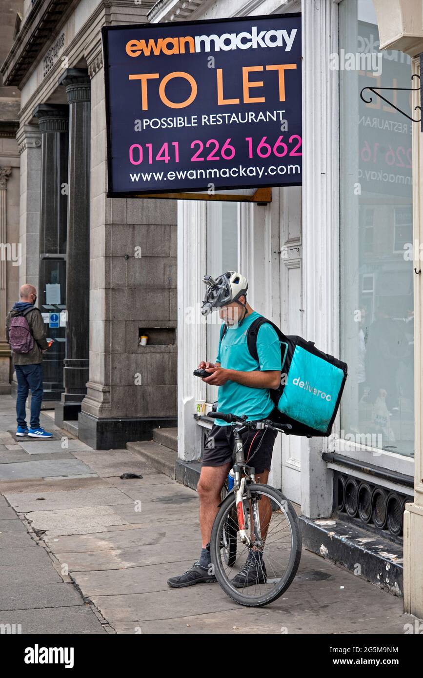 Um zu lassen, unterschreiben und Deliveroo Fahrer überprüfen sein Telefon auf Princes Street, Edinburgh, Schottland, Großbritannien. Stockfoto