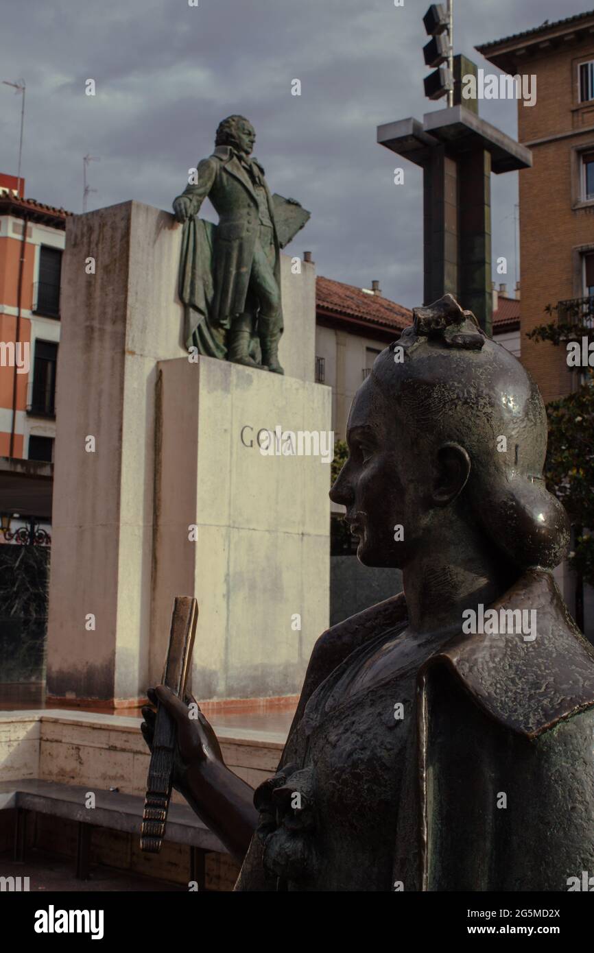 Statue einer jungen Frau auf dem Pilar-Platz in Zaragoza. Verschwommene Goya-Statue im Hintergrund Stockfoto