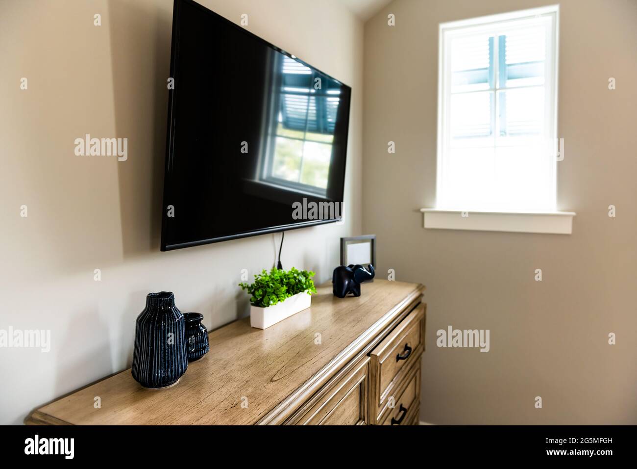 Tisch im kleinen Wohnzimmer oder Schlafzimmer mit stilvoller Gestaltung und niemand im Haus mit Fernseher an der Wand und neutralen Farben Stockfoto