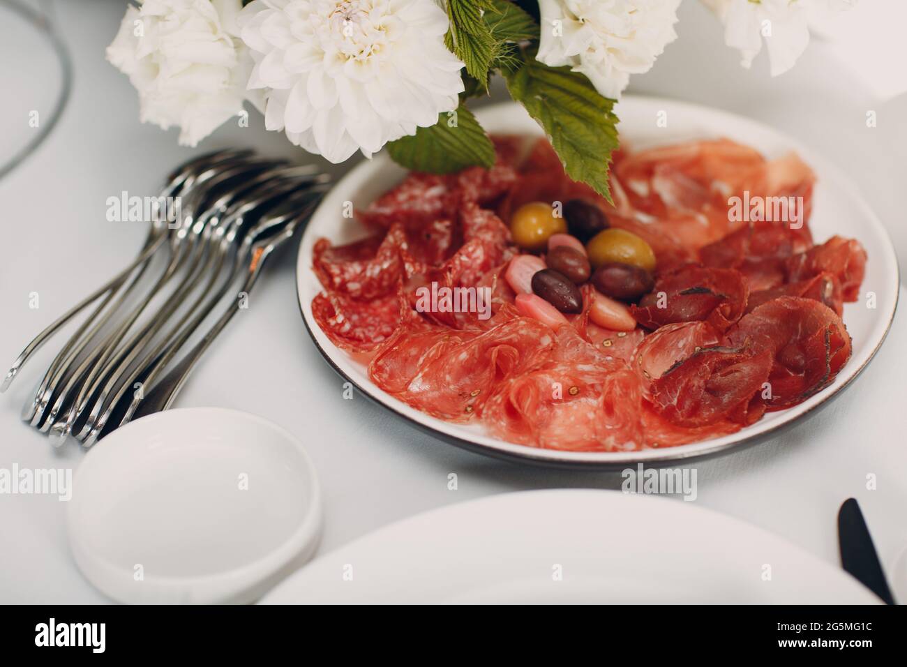 Verschiedene Aufschnitte auf einem Teller mit weißen Blumen auf dem Tisch. Stockfoto