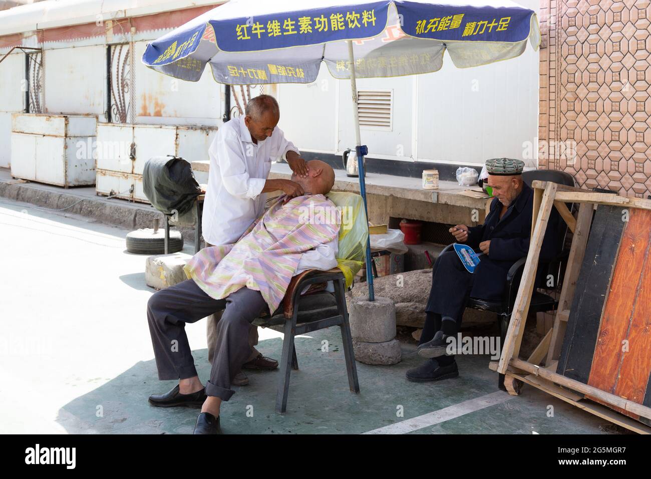 Ein Friseur rasiert einen Kunden in der Öffentlichkeit unter einem Regenschirm Stockfoto