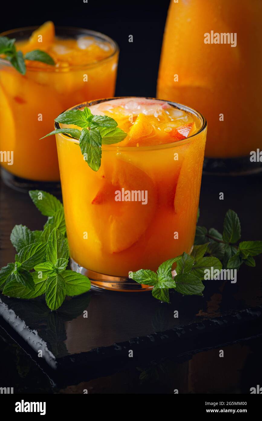 Kalte Getränke im Sommer: Hausgemachte Pfirsich-Sangria mit Eis und Minze im Glas auf schwarzem Hintergrund aus Holz Stockfoto