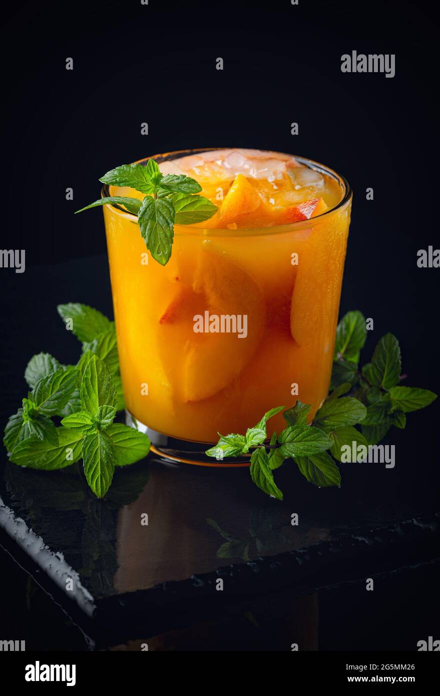 Kalte Getränke im Sommer: Hausgemachte Pfirsich-Sangria mit Eis und Minze im Glas auf schwarzem Hintergrund aus Holz Stockfoto