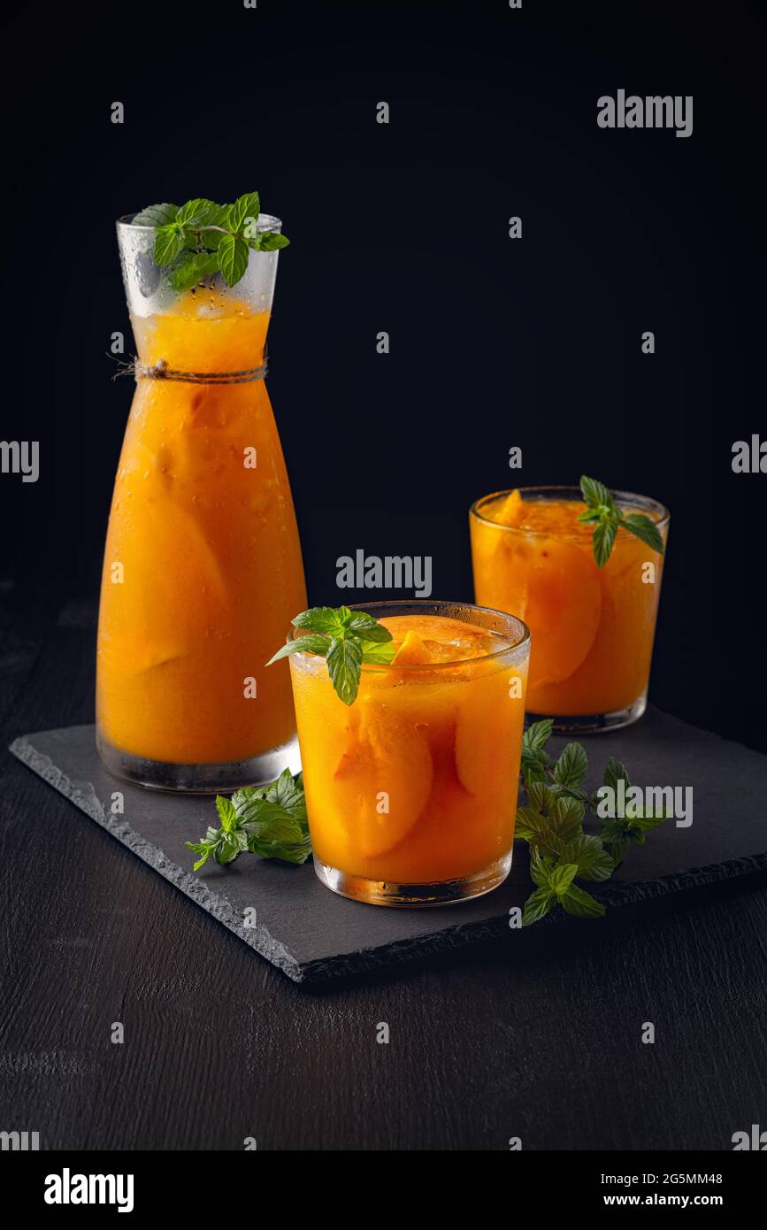 Kalte Getränke im Sommer: Hausgemachte Pfirsich-Sangria mit Eis und Minze im Glas auf schwarzem Holzhintergrundsommerliche kalte Getränke: Hausgemachte Pfirsich-Sangria mit Eis Stockfoto