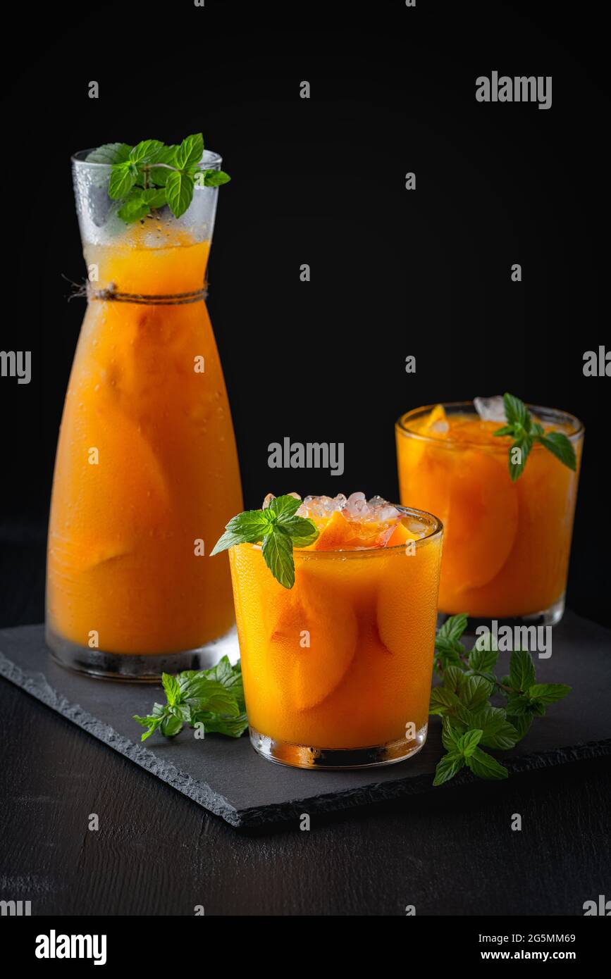 Kalte Getränke im Sommer: Hausgemachte Pfirsich-Sangria mit Eis und Minze im Glas auf schwarzem Hintergrund aus Holz Stockfoto