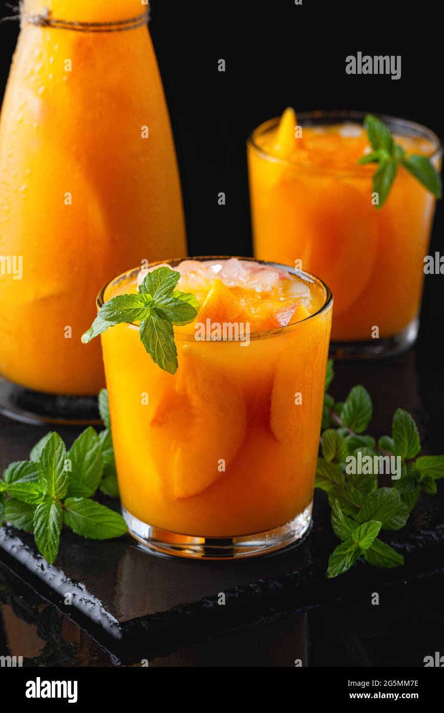 Kalte Getränke im Sommer: Hausgemachte Pfirsich-Sangria mit Eis und Minze im Glas auf schwarzem Hintergrund aus Holz Stockfoto