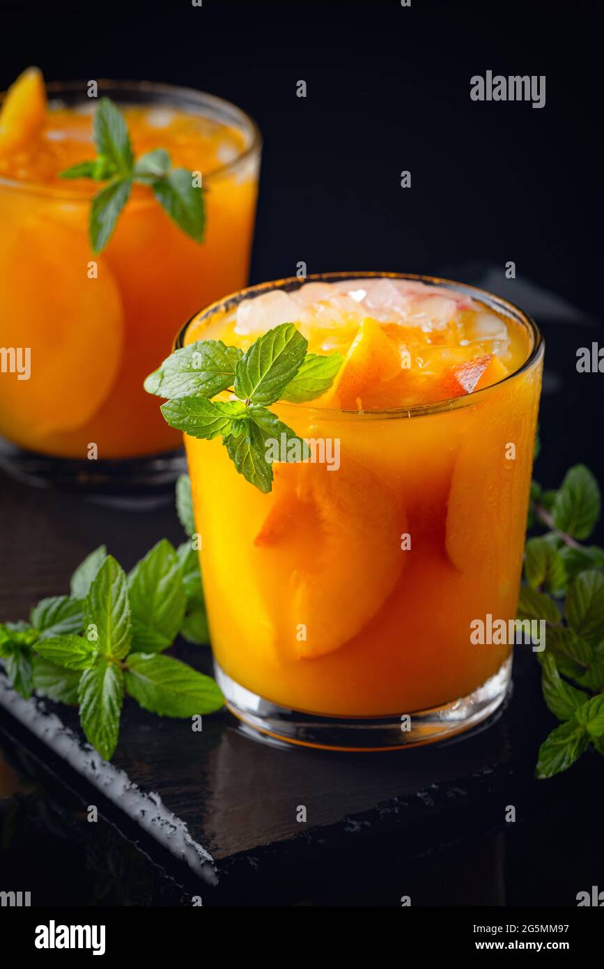 Kalte Getränke im Sommer: Hausgemachte Pfirsich-Sangria mit Eis und Minze im Glas auf schwarzem Hintergrund aus Holz Stockfoto