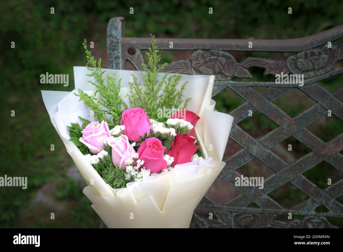Auf einem rustikalen Stahlstuhl ruhen Bouquet aus frischen roten und rosafarbenen Rosen. Speicherplatz kopieren. Stockfoto
