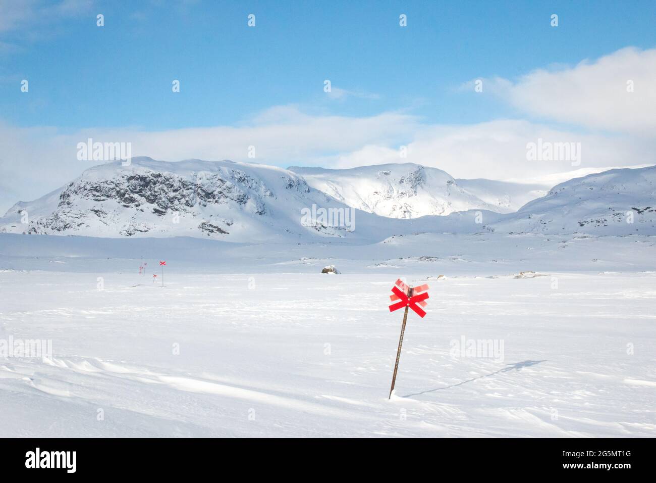 Verlassen der Alesjaure-Hütten bei Sonnenaufgang, während Schneeschuhwanderungen auf dem unberührten Kungsleden Trail, Lappland, Schweden, April 2021. Rote Kreuze markieren den Weg. Stockfoto