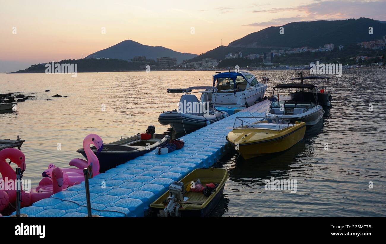 Schöner Sonnenuntergang am Meer. Vergnügungsboote und Yachten am Pier. Liegeponton aus blauen Kunststoffblöcken. Berge im Hintergrund. Stockfoto